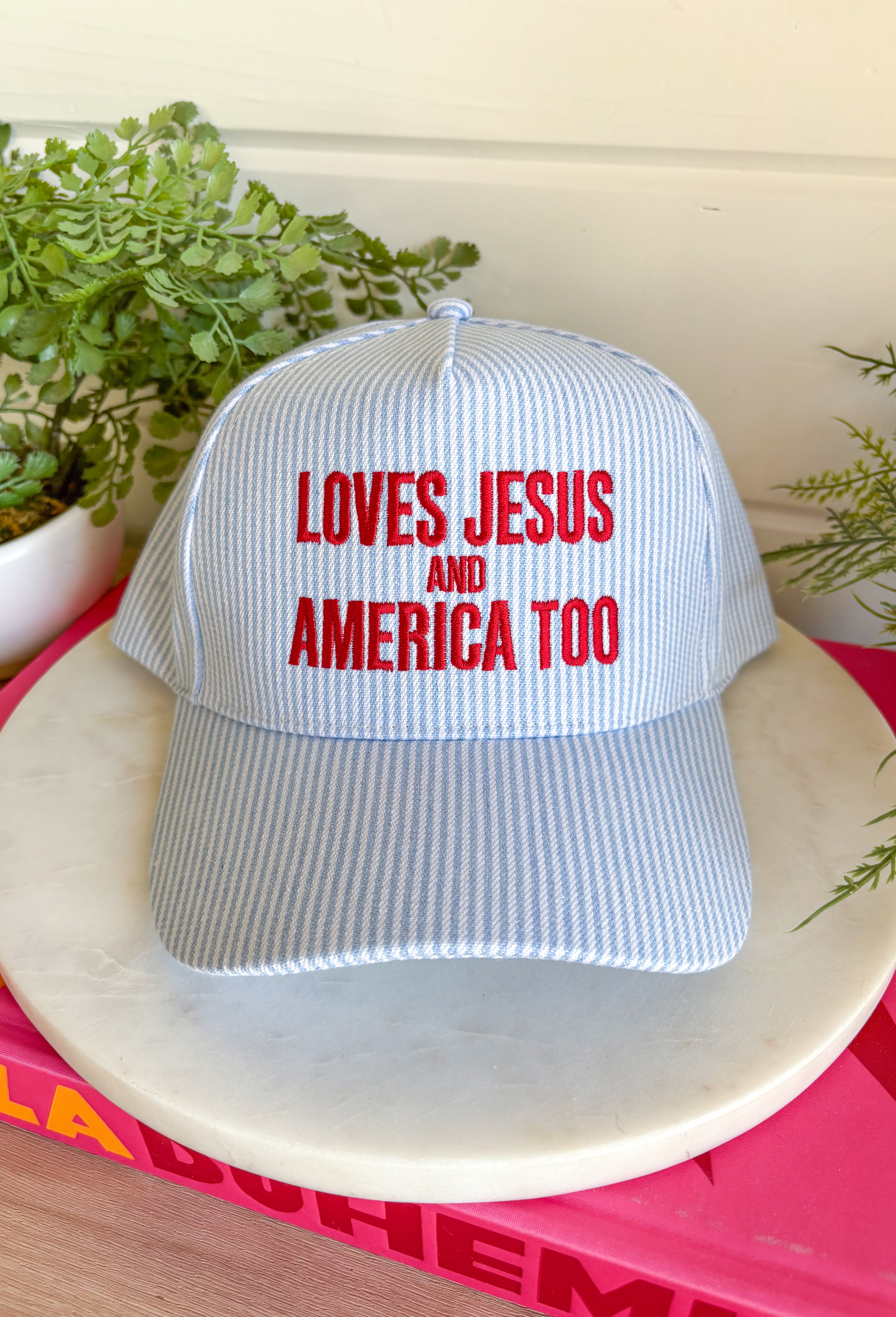 This light blue and white stripe trucker hat is made for celebrating faith, freedom, and all the 4th of July fun! Featuring “Loves Jesus And America Too” embroidered in red, it brings the perfect mix of patriotic spirit and meaningful style. The striped design keeps it fresh and festive, while the adjustable fit makes it easy to wear all day—from parades and lake days to backyard BBQs and fireworks. It’s the kind of hat that adds personality to any casual outfit and feels right at home all summer long. 