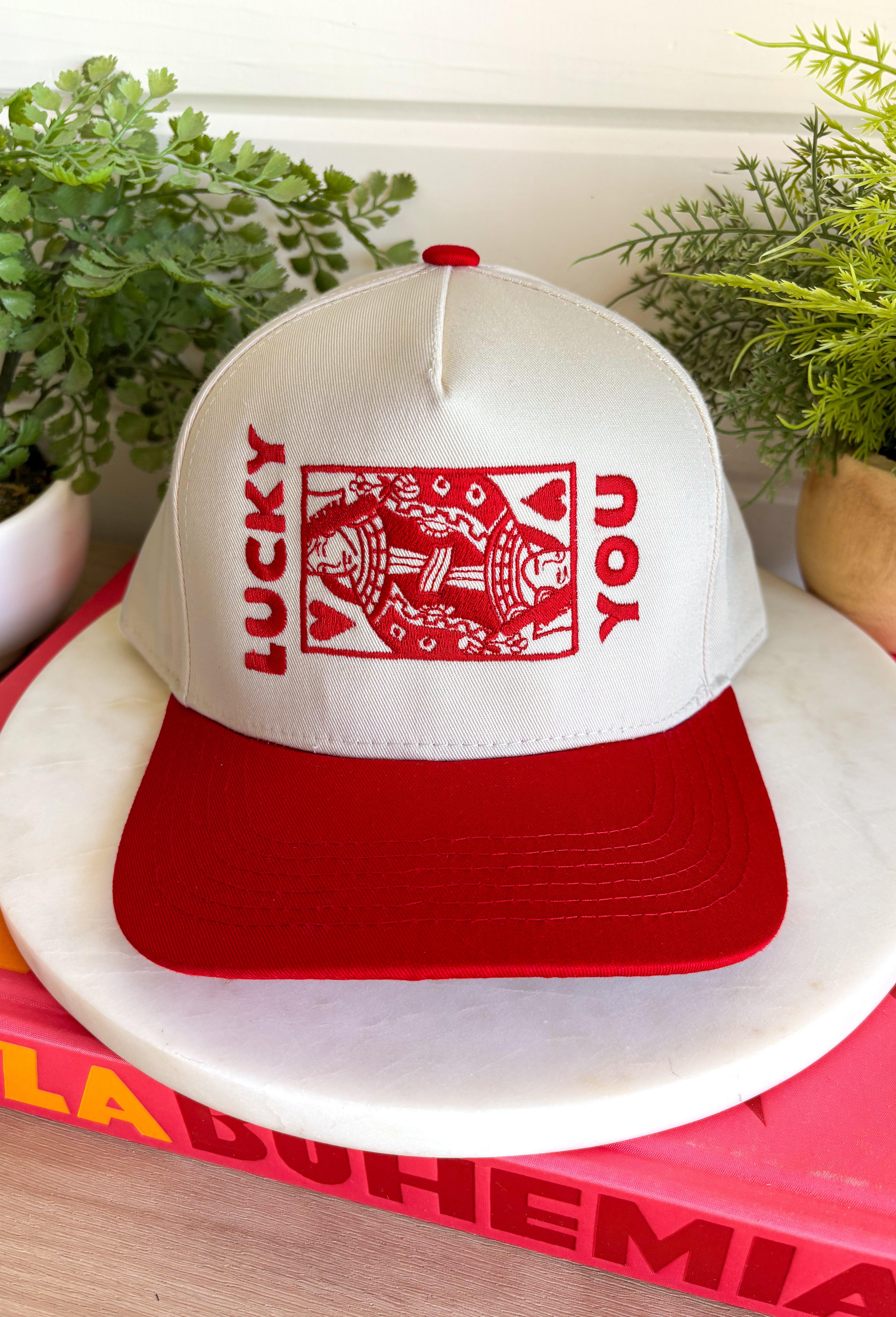 Feeling lucky? This trucker hat is the perfect blend of playful and classic, featuring "Lucky You" embroidered in red alongside a detailed playing card design on the front. The neutral crown and bold red bill create an eye-catching contrast that's easy to style for everyday wear. With its fun, casino-inspired graphic and adjustable fit, it's the perfect accessory for game nights, weekend outings, concerts, or simply adding a little personality to your look.