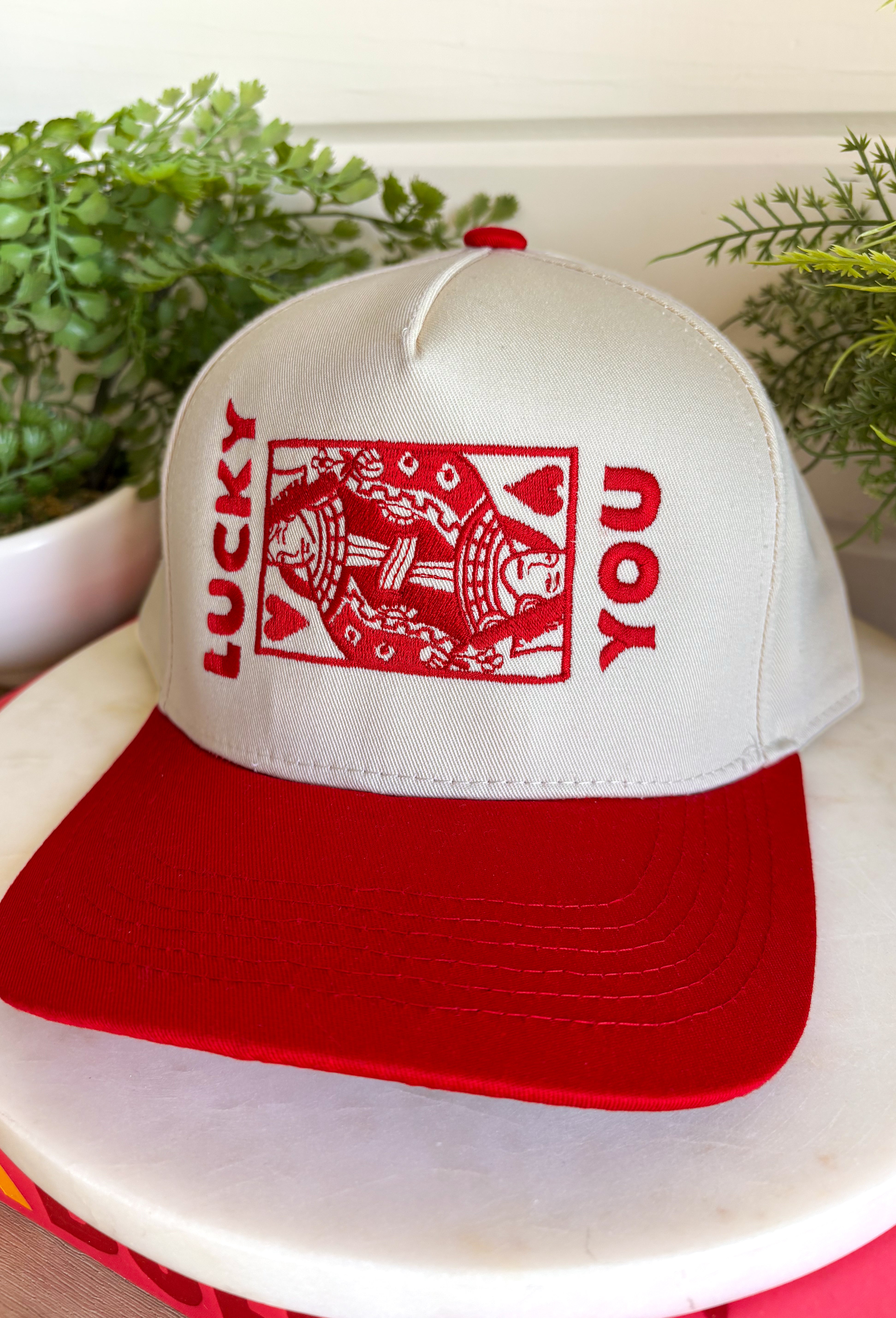 Feeling lucky? This trucker hat is the perfect blend of playful and classic, featuring "Lucky You" embroidered in red alongside a detailed playing card design on the front. The neutral crown and bold red bill create an eye-catching contrast that's easy to style for everyday wear. With its fun, casino-inspired graphic and adjustable fit, it's the perfect accessory for game nights, weekend outings, concerts, or simply adding a little personality to your look.
