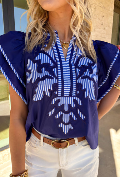 Classic with a fun spring twist, this short sleeve navy top by Entro is an easy everyday favorite. Featuring a bold blue and white stripe motif on the front, it adds the perfect pop of pattern while still feeling clean and timeless. Matching blue and white stripe trim throughout gives it an extra polished touch, making it a simple top that still feels special. Lightweight and comfy, it pairs effortlessly with denim, shorts, or a crisp white skirt for spring.