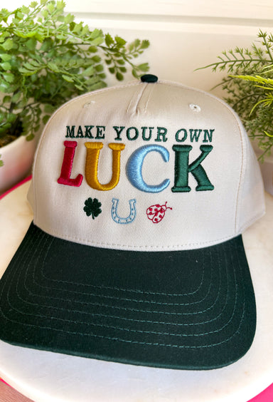 A little luck and a lot of style! This trucker hat features beautifully embroidered "Make Your Own Luck" lettering alongside a four-leaf clover, horseshoe, and ladybug in rich, eye-catching colors. The neutral crown paired with the dark green bill gives it a timeless look that's easy to style, while the detailed embroidery adds the perfect touch of personality. 