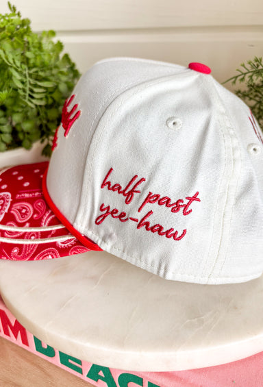 Bring a little western charm and plenty of personality to your everyday style with this fun trucker hat. Featuring a neutral front paired with a bold red bandana print bill, this standout accessory is embroidered with "Not Gonna Hold My Horses" across the front in vibrant red stitching. The side is finished with "Half Past Yee-Haw" embroidery, while a red embroidered horseshoe on the back adds the perfect finishing touch. 