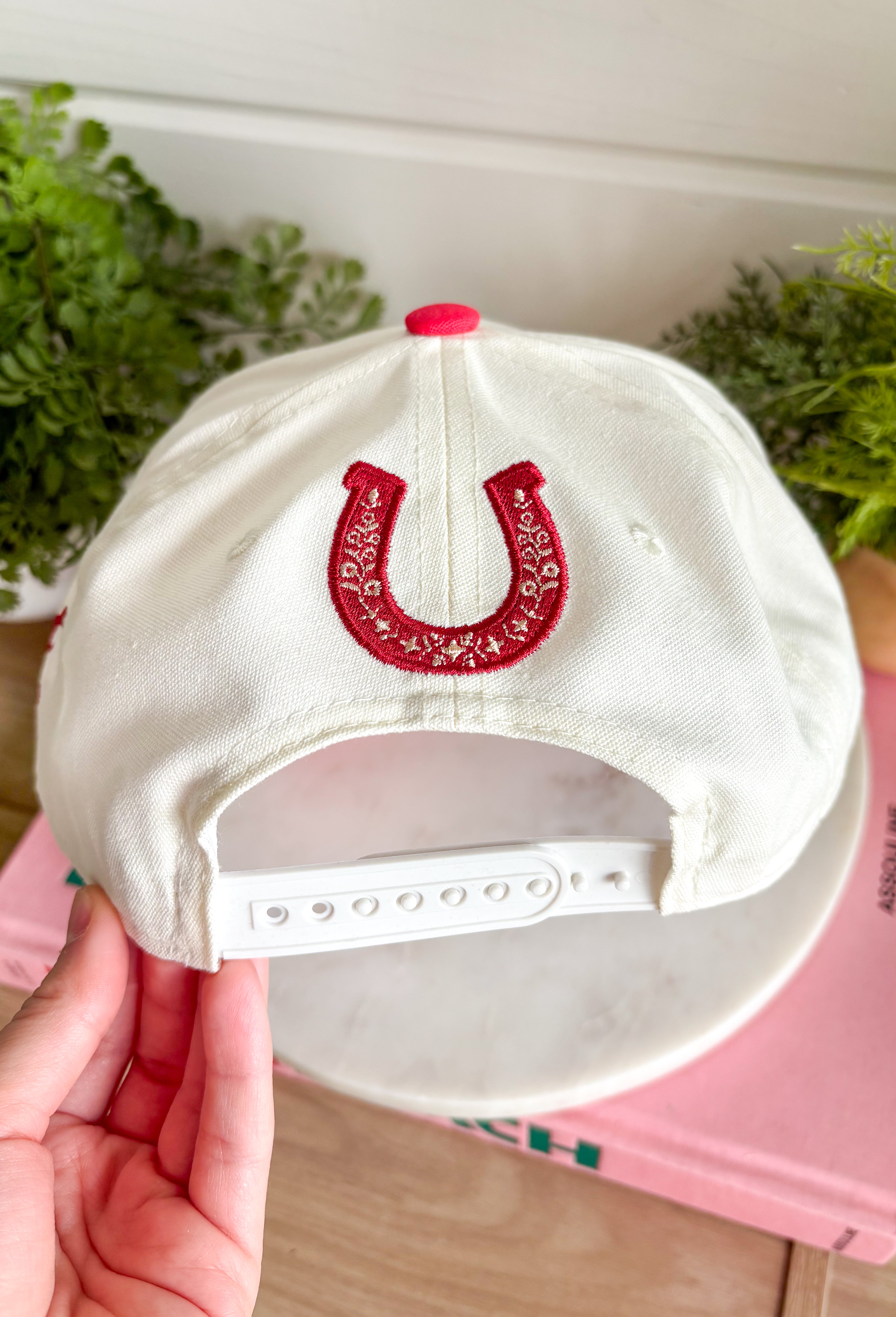 Bring a little western charm and plenty of personality to your everyday style with this fun trucker hat. Featuring a neutral front paired with a bold red bandana print bill, this standout accessory is embroidered with "Not Gonna Hold My Horses" across the front in vibrant red stitching. The side is finished with "Half Past Yee-Haw" embroidery, while a red embroidered horseshoe on the back adds the perfect finishing touch. 