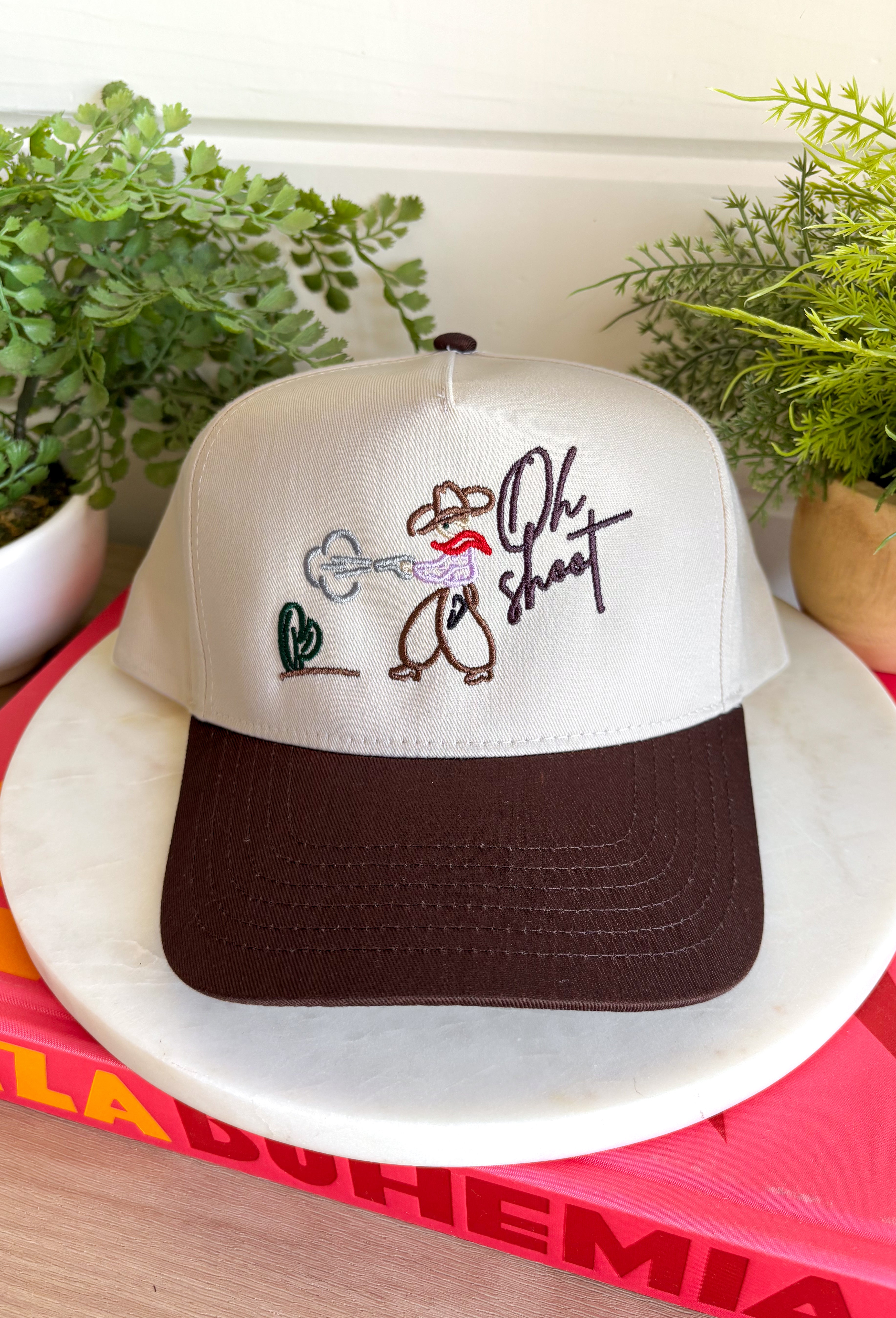This trucker hat brings the perfect mix of western charm and playful personality! Featuring an embroidered cowboy, cactus, and the phrase "Oh Shoot," it's a fun conversation starter that adds a little humor to any casual outfit. The neutral crown and brown bill make it easy to pair with just about everything, while the adjustable fit keeps it comfortable for all-day wear. 