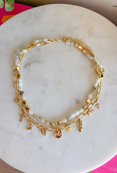 This layered necklace gives you that perfectly styled, on-trend look without any effort! Featuring a neutral beaded strand with gold accents paired with a charm-filled gold chain, it brings the perfect mix of western-inspired and playful details. With charms like a cross, heart, palm leaf, bow, and even a shoe, it adds so much personality to your outfit. Lightweight and easy to wear, it’s the ultimate throw-on accessory for summer days when you want to look put together in seconds. 