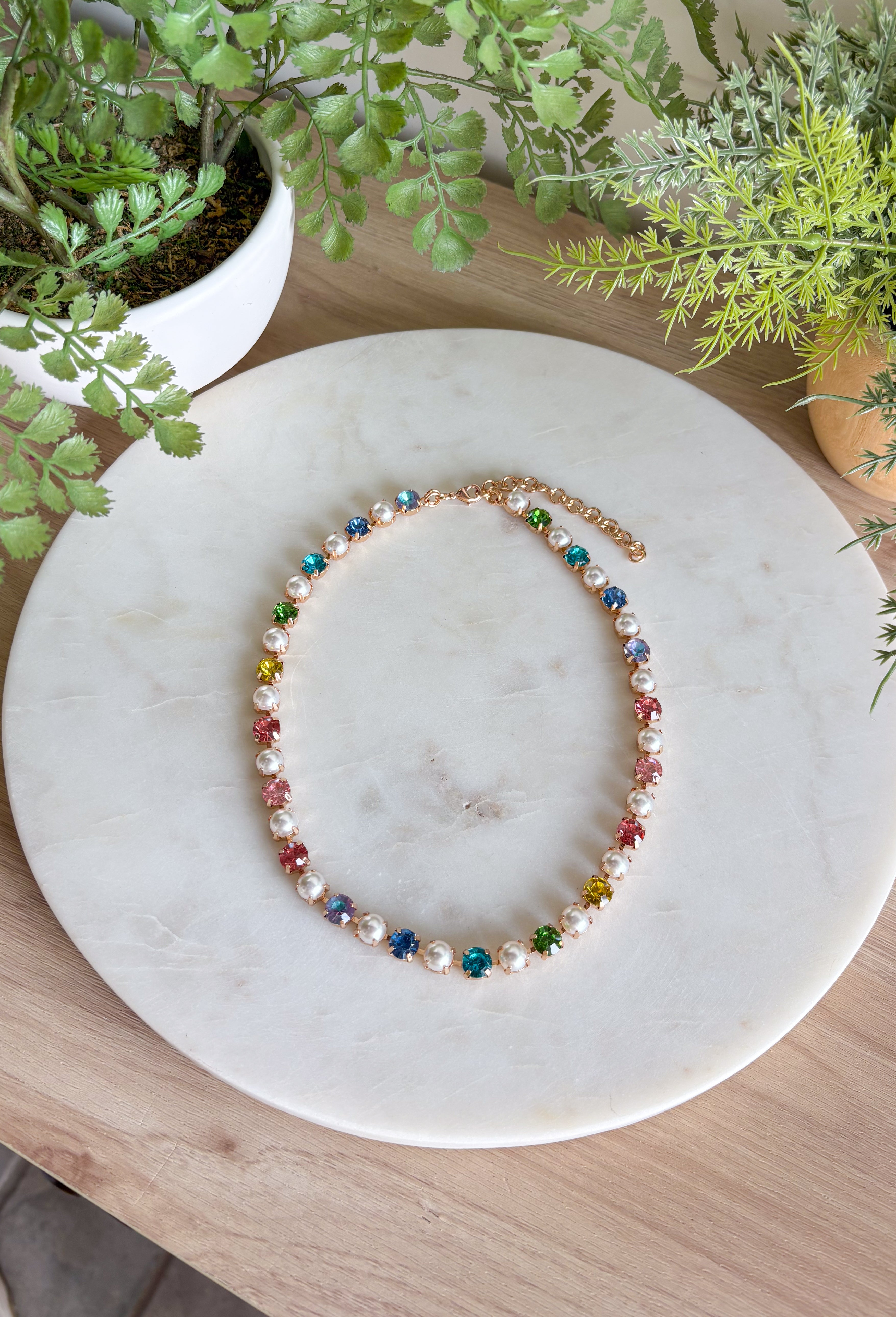 This pastel gemstone necklace brings a soft, dreamy touch to your spring accessory lineup. Featuring faceted crystal stones in gentle pastel hues, it’s beautifully accented with pearl details throughout for an added layer of elegance and charm. Each stone is set in a warm gold setting, giving the necklace a polished feel while still keeping it light and playful. It’s the perfect piece for brightening up everyday outfits or adding a romantic finishing touch to dresses and blouses.