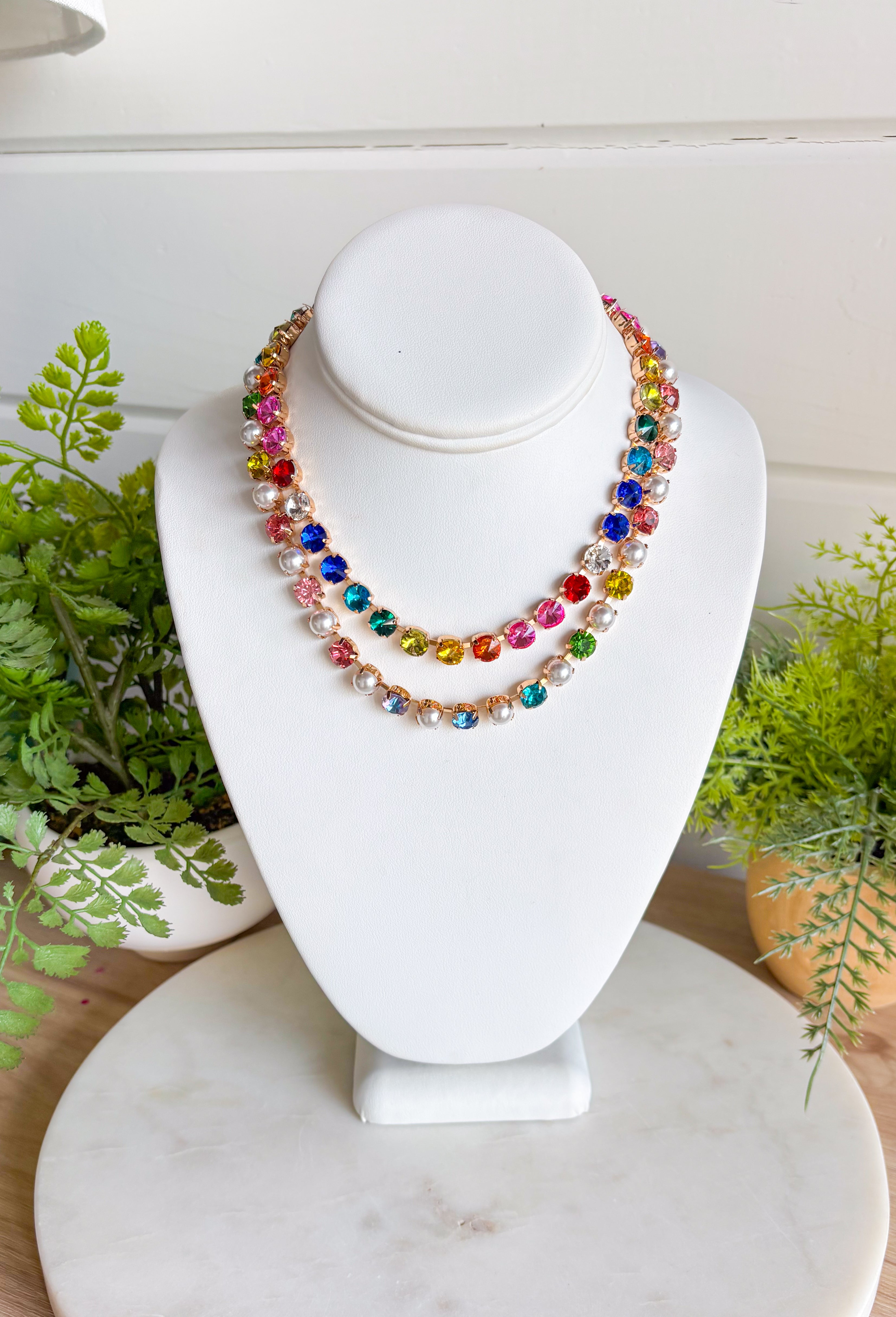 This pastel gemstone necklace brings a soft, dreamy touch to your spring accessory lineup. Featuring faceted crystal stones in gentle pastel hues, it’s beautifully accented with pearl details throughout for an added layer of elegance and charm. Each stone is set in a warm gold setting, giving the necklace a polished feel while still keeping it light and playful. It’s the perfect piece for brightening up everyday outfits or adding a romantic finishing touch to dresses and blouses.