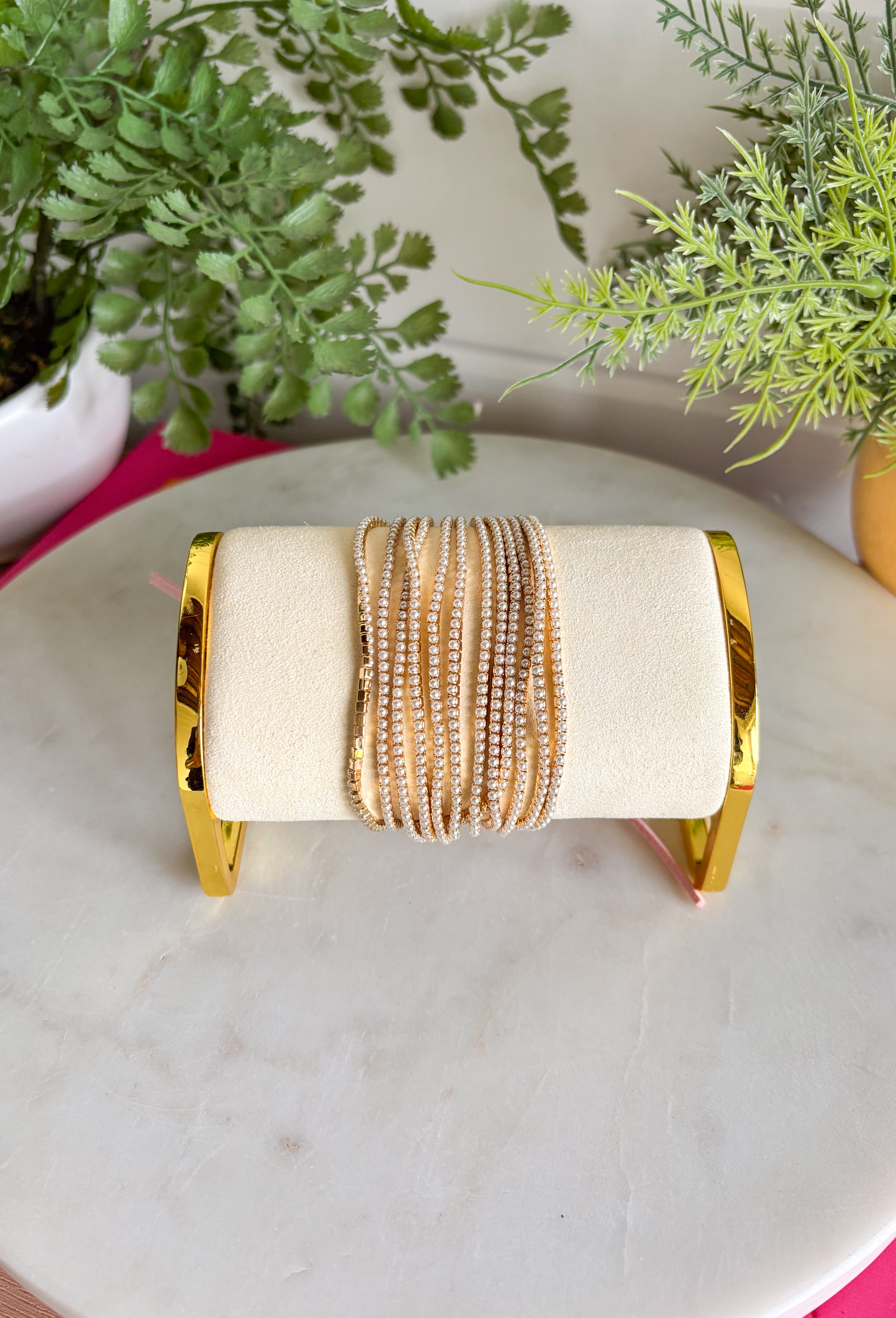 Delicate, timeless, and perfect for layering! This set of twelve dainty gold bracelets features subtle pearl accents throughout for a soft, feminine touch. The mix of polished gold and tiny pearls creates a look that feels effortlessly elegant while still being easy enough for everyday wear. Designed with a stretchy pull-on style, these bracelets are comfortable to slip on and stack together for a beautifully layered look. 