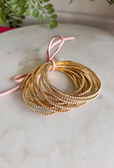 Delicate, timeless, and perfect for layering! This set of twelve dainty gold bracelets features subtle pearl accents throughout for a soft, feminine touch. The mix of polished gold and tiny pearls creates a look that feels effortlessly elegant while still being easy enough for everyday wear. Designed with a stretchy pull-on style, these bracelets are comfortable to slip on and stack together for a beautifully layered look. 