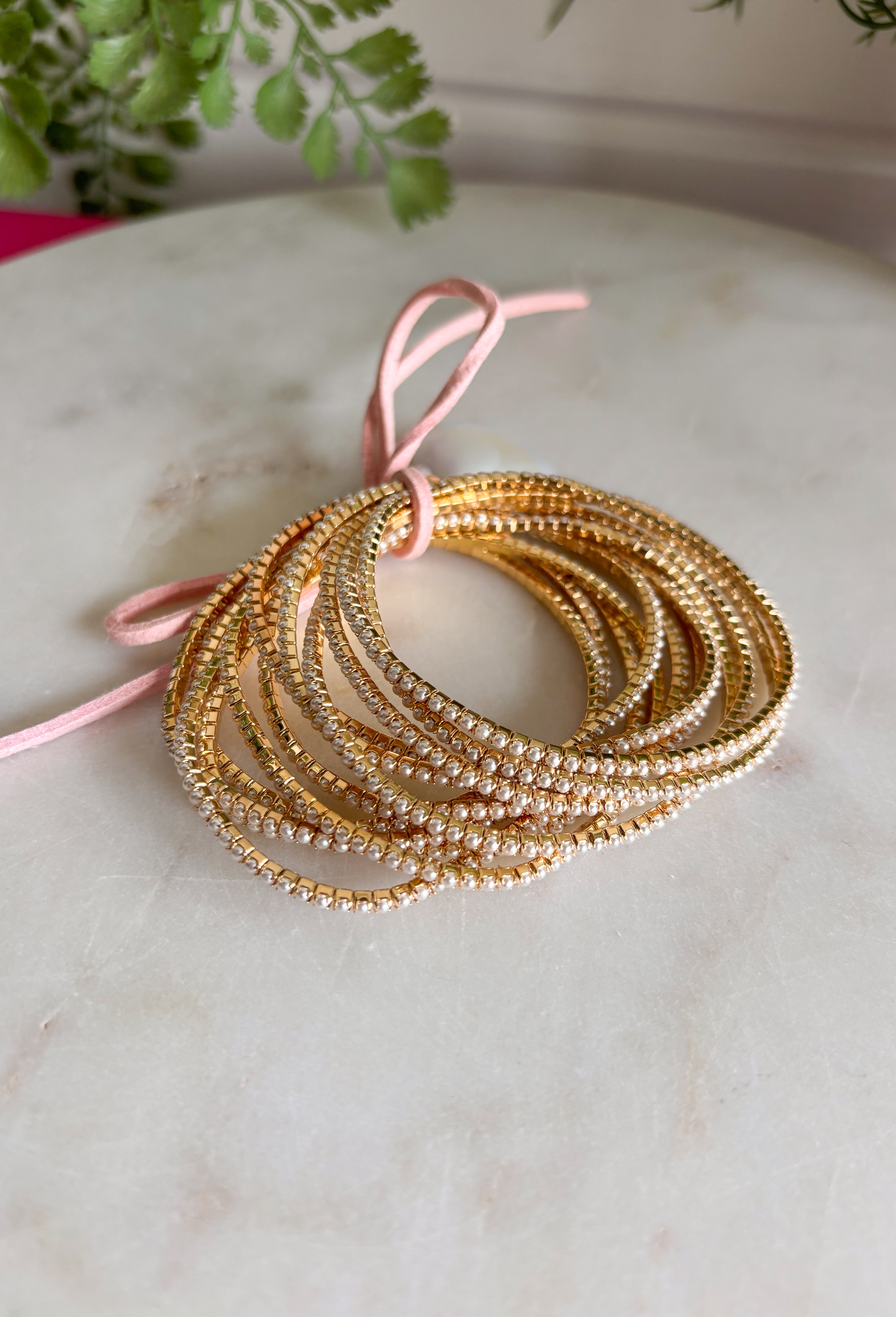 Delicate, timeless, and perfect for layering! This set of twelve dainty gold bracelets features subtle pearl accents throughout for a soft, feminine touch. The mix of polished gold and tiny pearls creates a look that feels effortlessly elegant while still being easy enough for everyday wear. Designed with a stretchy pull-on style, these bracelets are comfortable to slip on and stack together for a beautifully layered look. 