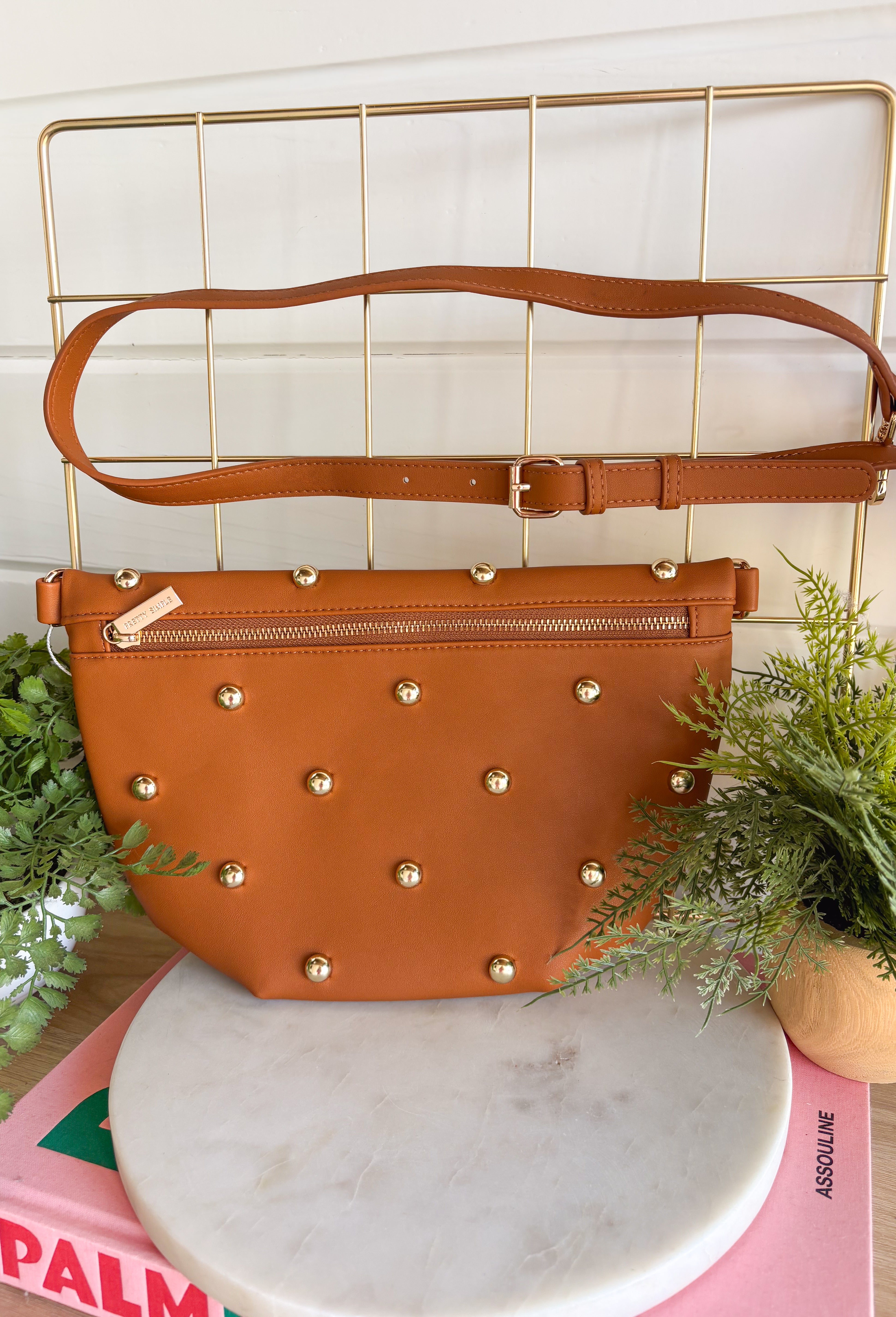 Everyone's favorite bag is back in a bold new design! The Studded Westlyn Bum Bag from Pretty Simple features the same hands-free style you love, now updated with eye-catching gold stud detailing for the perfect touch of edge. Crafted from soft vegan leather, this versatile bag can be worn as a belt bag or crossbody, making it the perfect companion for busy days, concerts, travel, shopping, and everyday adventures. Stylish, functional, and easy to wear, it's sure to become your new go-to accessory.
