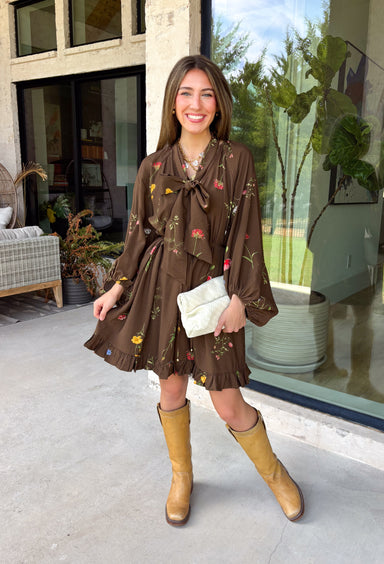 Feminine, chic, and full of seasonal charm, this floral dress is the perfect piece for all your favorite fall occasions. Featuring a classic brown backdrop with a vibrant colorful floral print, this dress offers a timeless silhouette with eye-catching details. The flattering v-neckline is accented by a beautiful scarf tie that adds a polished, sophisticated touch, while the self-tie waist creates a customizable fit you'll love. 