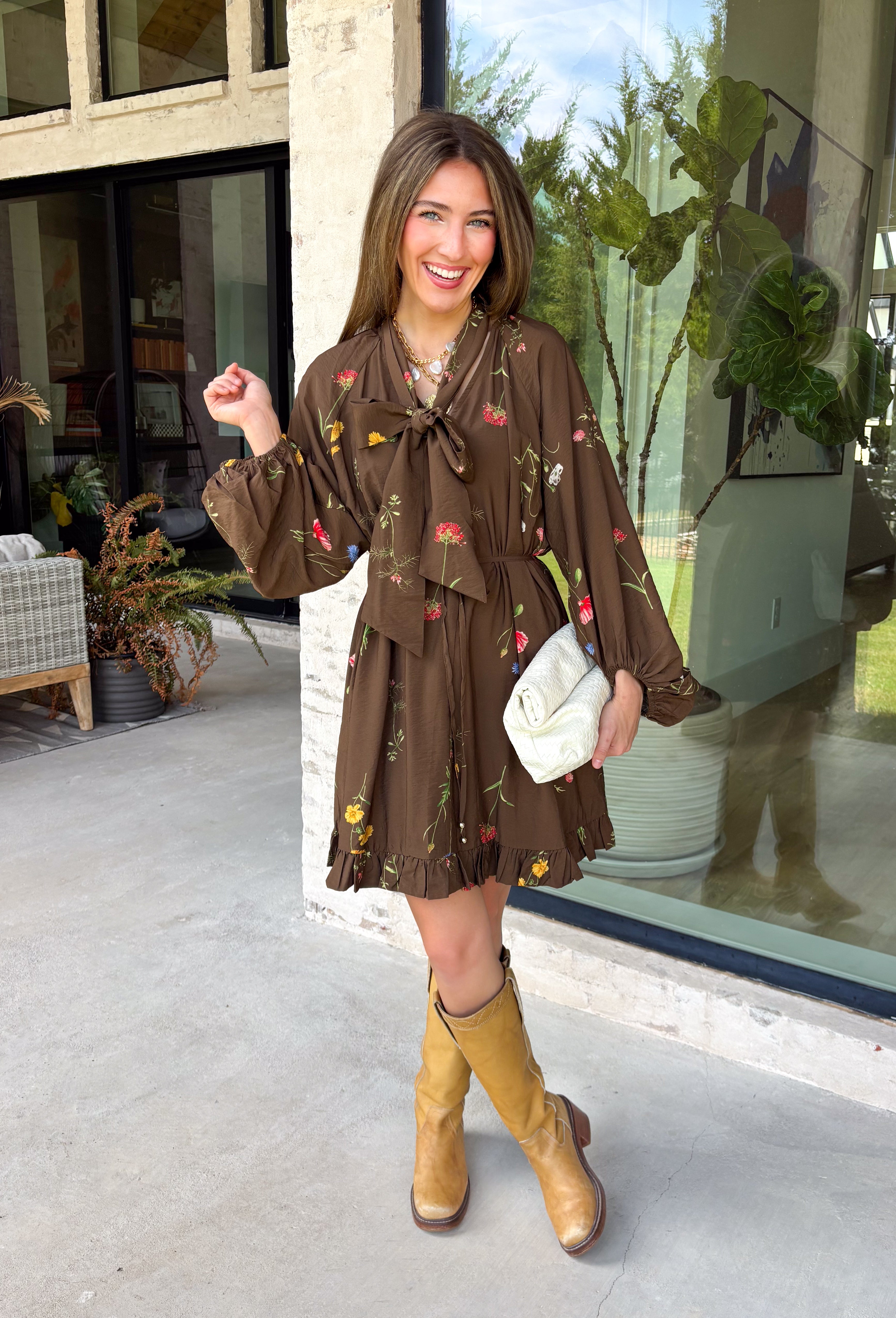 Feminine, chic, and full of seasonal charm, this floral dress is the perfect piece for all your favorite fall occasions. Featuring a classic brown backdrop with a vibrant colorful floral print, this dress offers a timeless silhouette with eye-catching details. The flattering v-neckline is accented by a beautiful scarf tie that adds a polished, sophisticated touch, while the self-tie waist creates a customizable fit you'll love. 