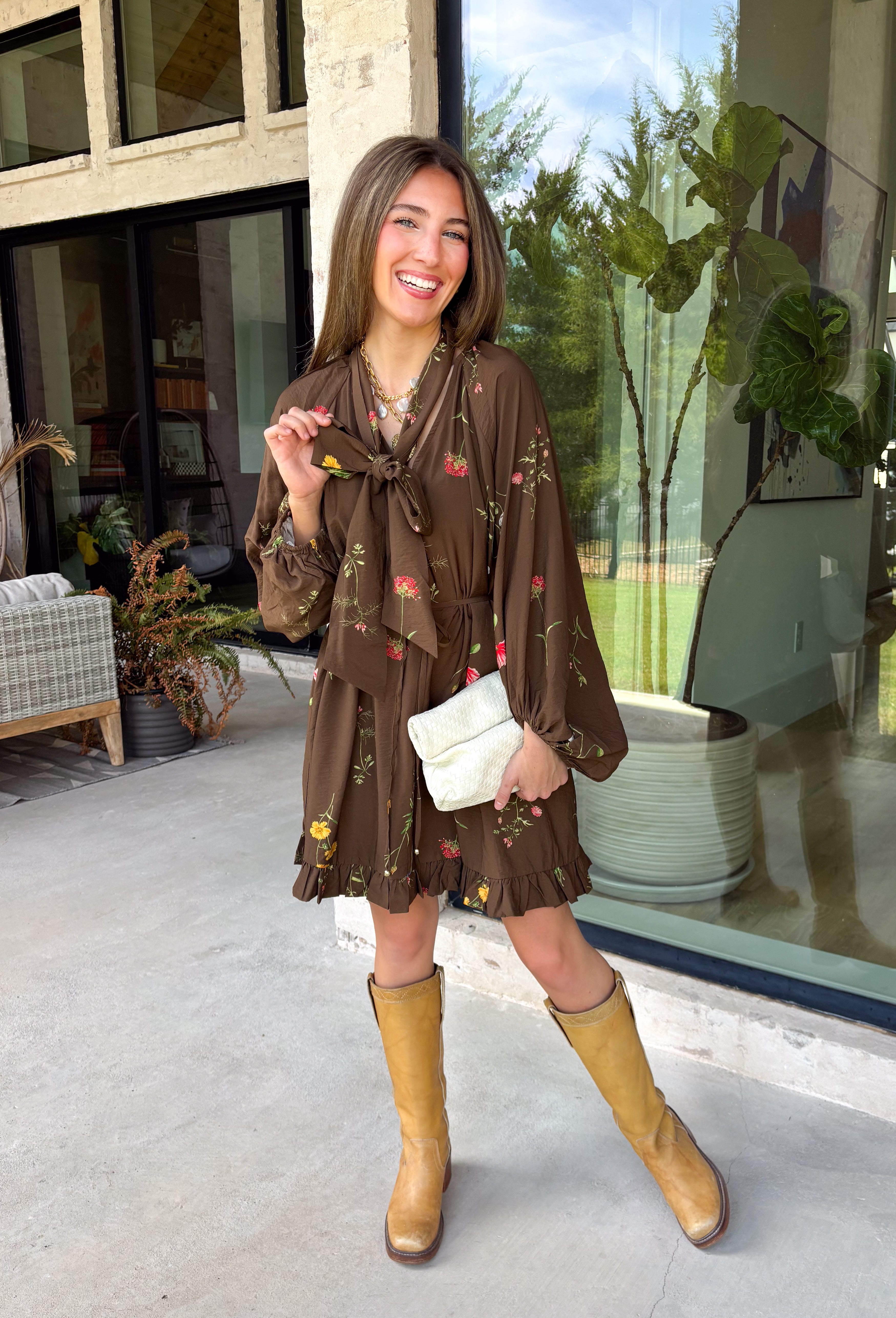 Feminine, chic, and full of seasonal charm, this floral dress is the perfect piece for all your favorite fall occasions. Featuring a classic brown backdrop with a vibrant colorful floral print, this dress offers a timeless silhouette with eye-catching details. The flattering v-neckline is accented by a beautiful scarf tie that adds a polished, sophisticated touch, while the self-tie waist creates a customizable fit you'll love. 