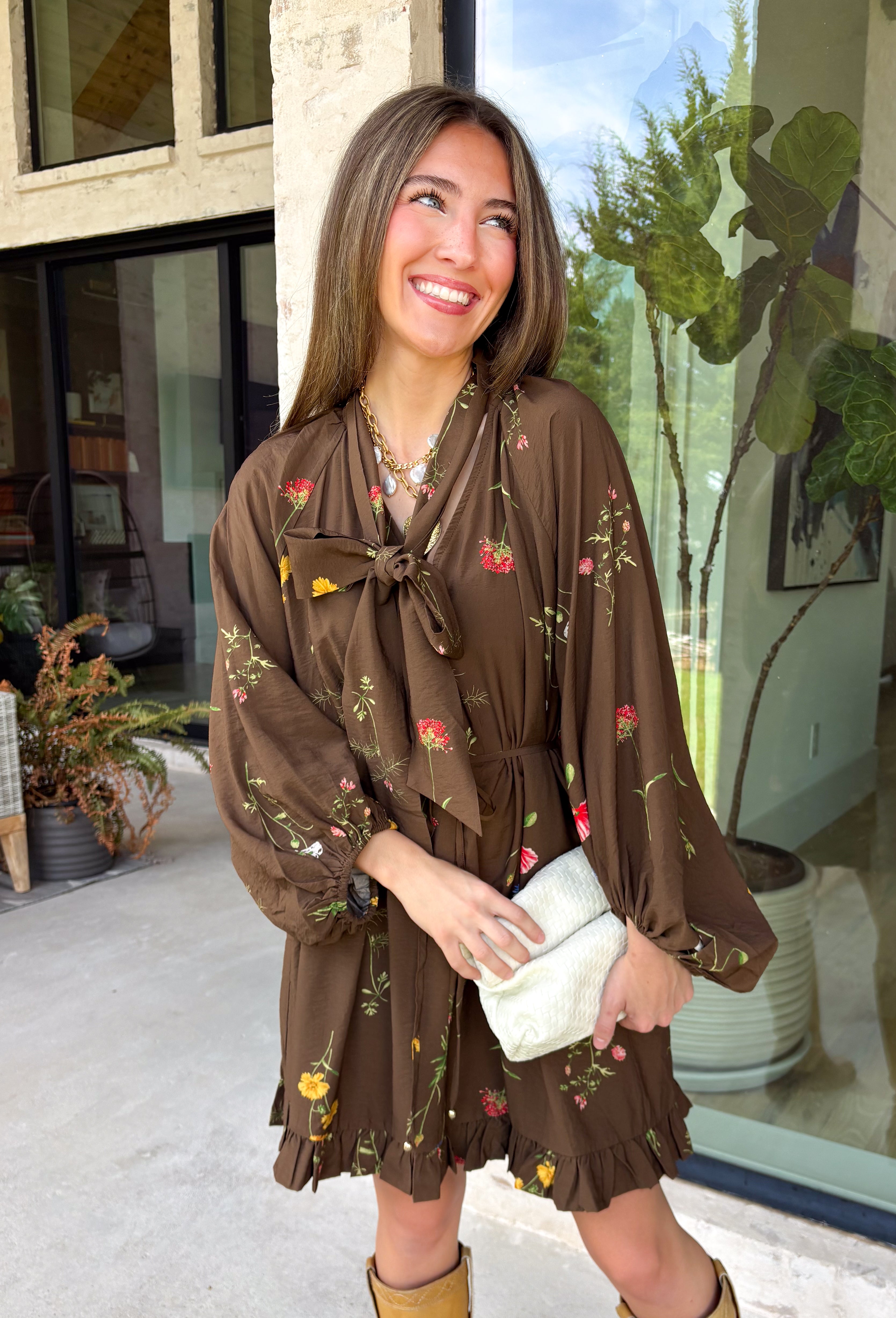 Feminine, chic, and full of seasonal charm, this floral dress is the perfect piece for all your favorite fall occasions. Featuring a classic brown backdrop with a vibrant colorful floral print, this dress offers a timeless silhouette with eye-catching details. The flattering v-neckline is accented by a beautiful scarf tie that adds a polished, sophisticated touch, while the self-tie waist creates a customizable fit you'll love. 
