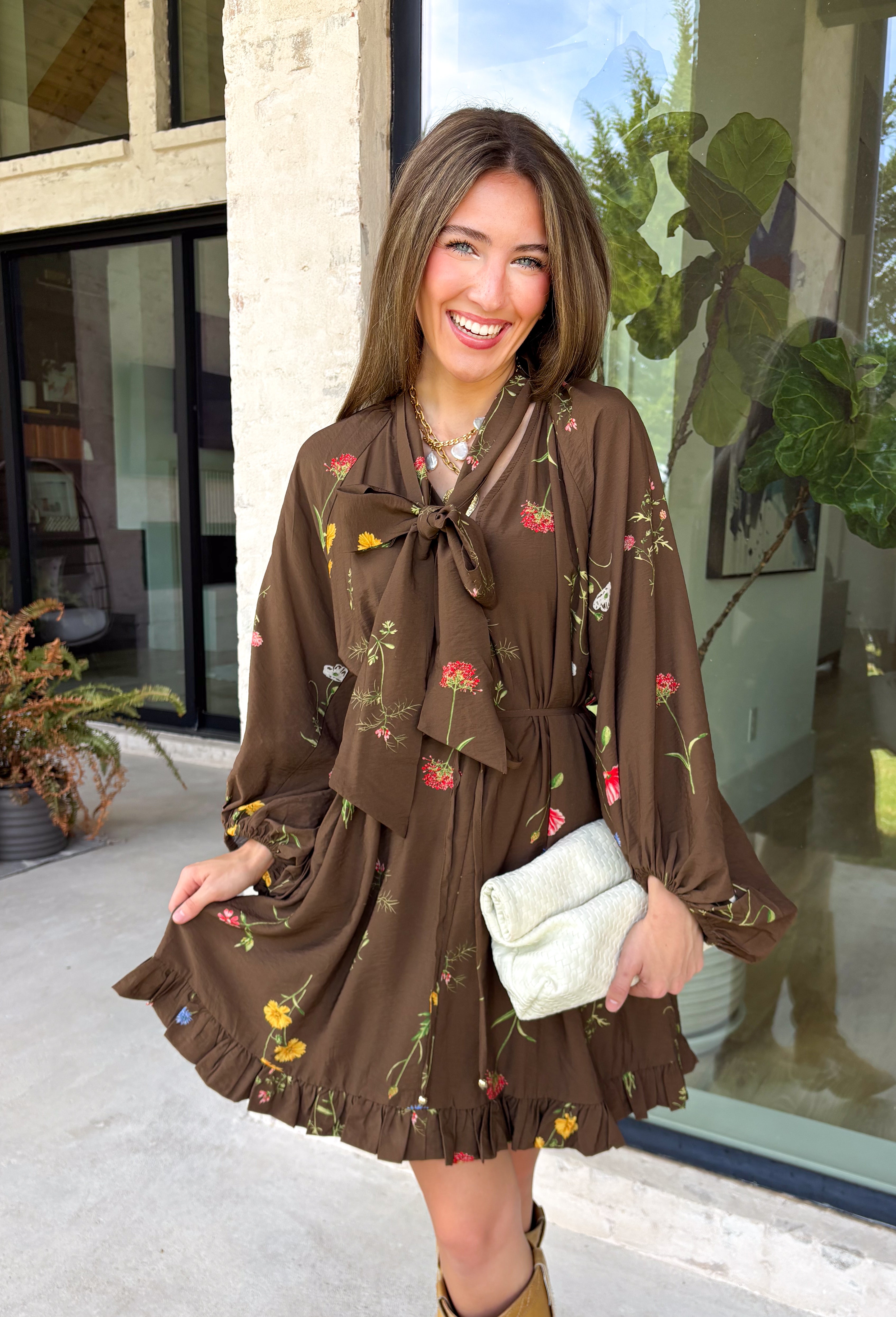 Feminine, chic, and full of seasonal charm, this floral dress is the perfect piece for all your favorite fall occasions. Featuring a classic brown backdrop with a vibrant colorful floral print, this dress offers a timeless silhouette with eye-catching details. The flattering v-neckline is accented by a beautiful scarf tie that adds a polished, sophisticated touch, while the self-tie waist creates a customizable fit you'll love. 