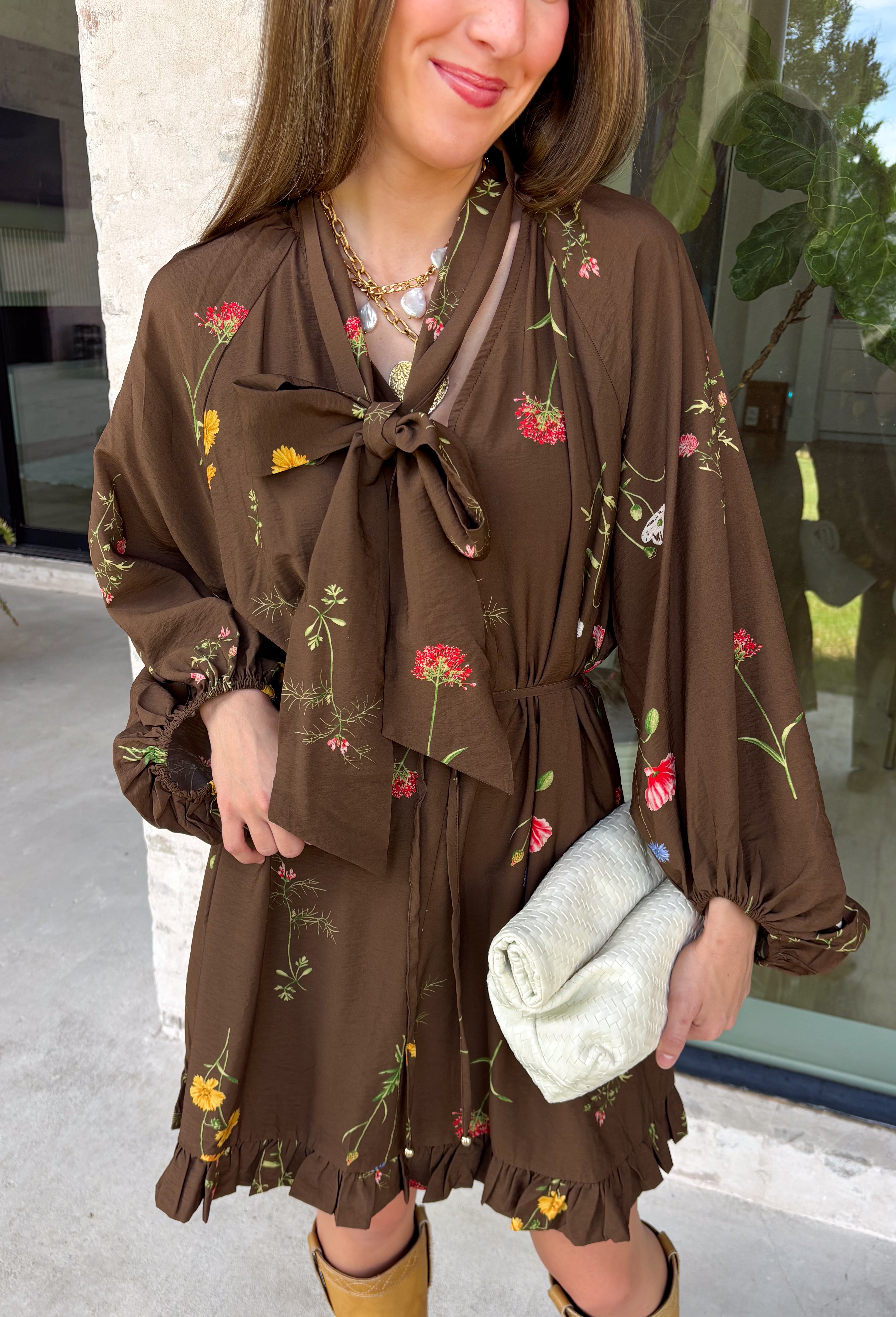 Feminine, chic, and full of seasonal charm, this floral dress is the perfect piece for all your favorite fall occasions. Featuring a classic brown backdrop with a vibrant colorful floral print, this dress offers a timeless silhouette with eye-catching details. The flattering v-neckline is accented by a beautiful scarf tie that adds a polished, sophisticated touch, while the self-tie waist creates a customizable fit you'll love. 