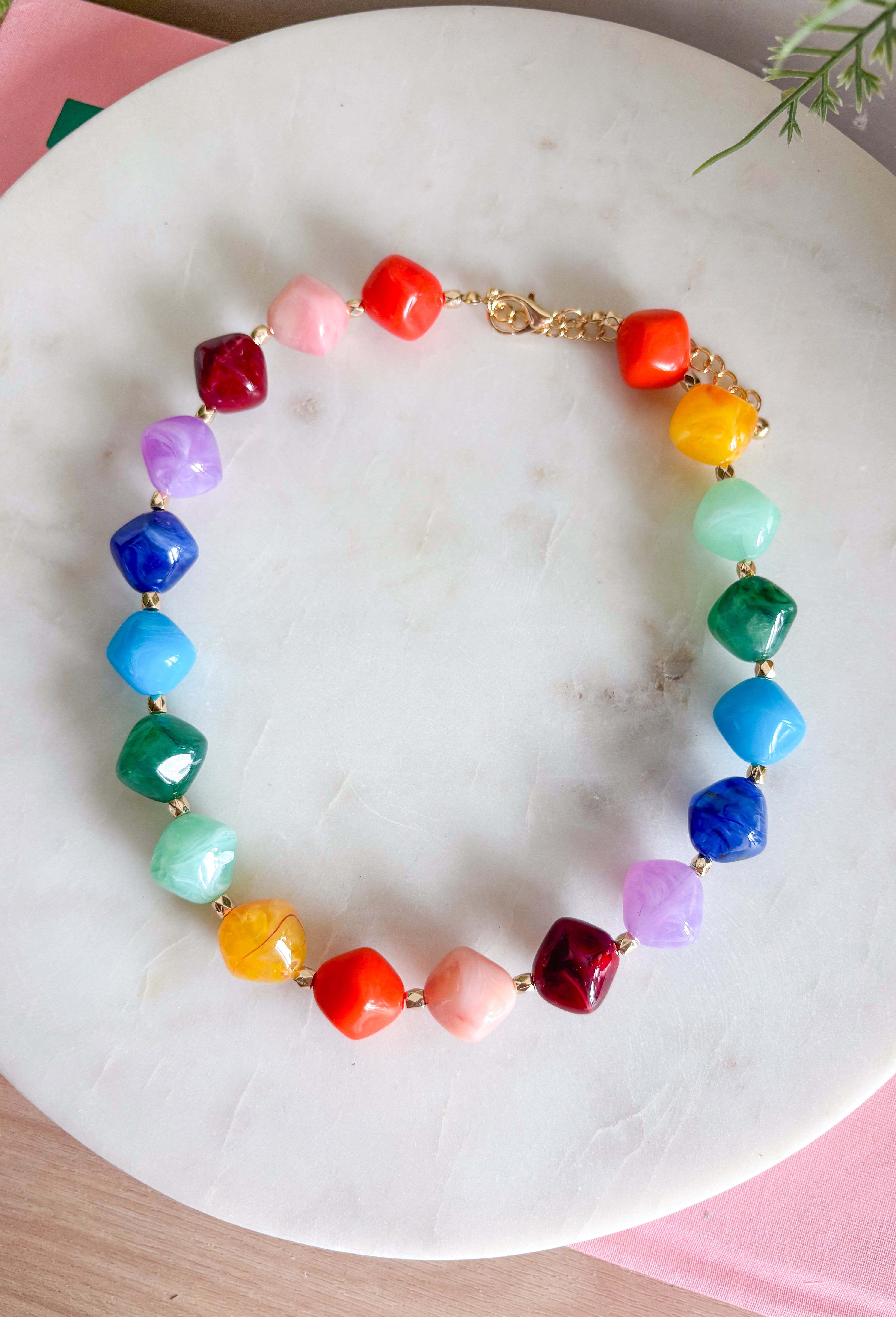 Brighten up any outfit with this colorful chunky beaded necklace that's full of personality and charm. Featuring vibrant beads in shades of navy, blue, green, purple, orange, yellow, and burgundy, this eye-catching accessory is accented with polished gold beads throughout for the perfect hint of shine. The versatile design makes it easy to wear with everything from casual sweaters to your favorite dresses, adding a fun pop of color wherever you go.