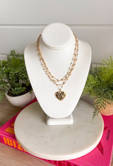 An effortless layered look with a sweet touch of shine! This gold layered necklace features delicate strands with small gold beads throughout, finished with a textured gold heart pendant that adds just the right amount of charm. The layered design makes styling easy—giving you that perfectly stacked look in one simple piece. Whether worn with a casual outfit or dressed up for a special moment, this necklace adds a soft, feminine glow to any look.