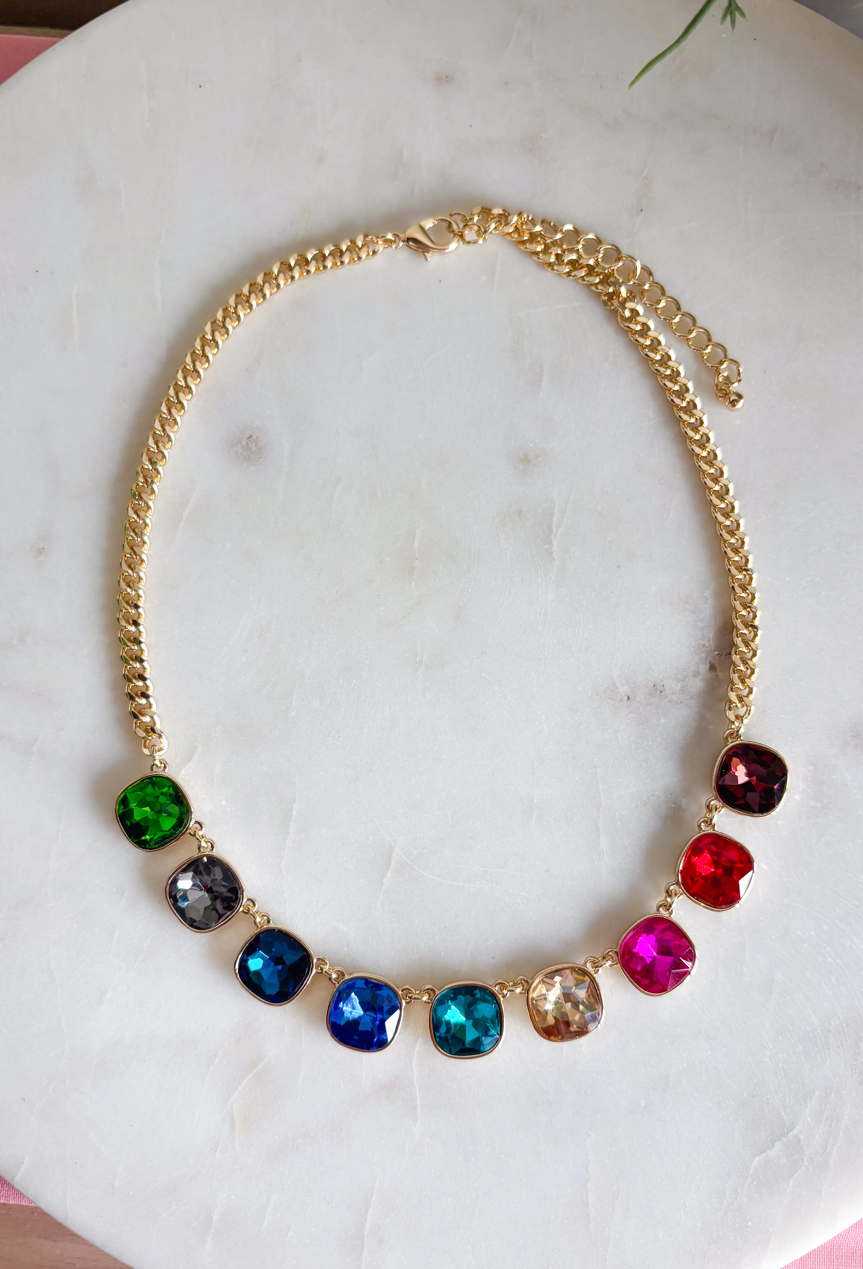 Add a vibrant finishing touch to your jewelry collection with this stunning gold chain necklace. Featuring colorful gemstones in shades of green, blue, gold, pink, red, and burgundy, this chic piece brings the perfect balance of timeless style and playful color. The delicate gold chain makes it easy to wear on its own or layered with your favorite necklaces, creating an effortlessly polished look for any occasion.