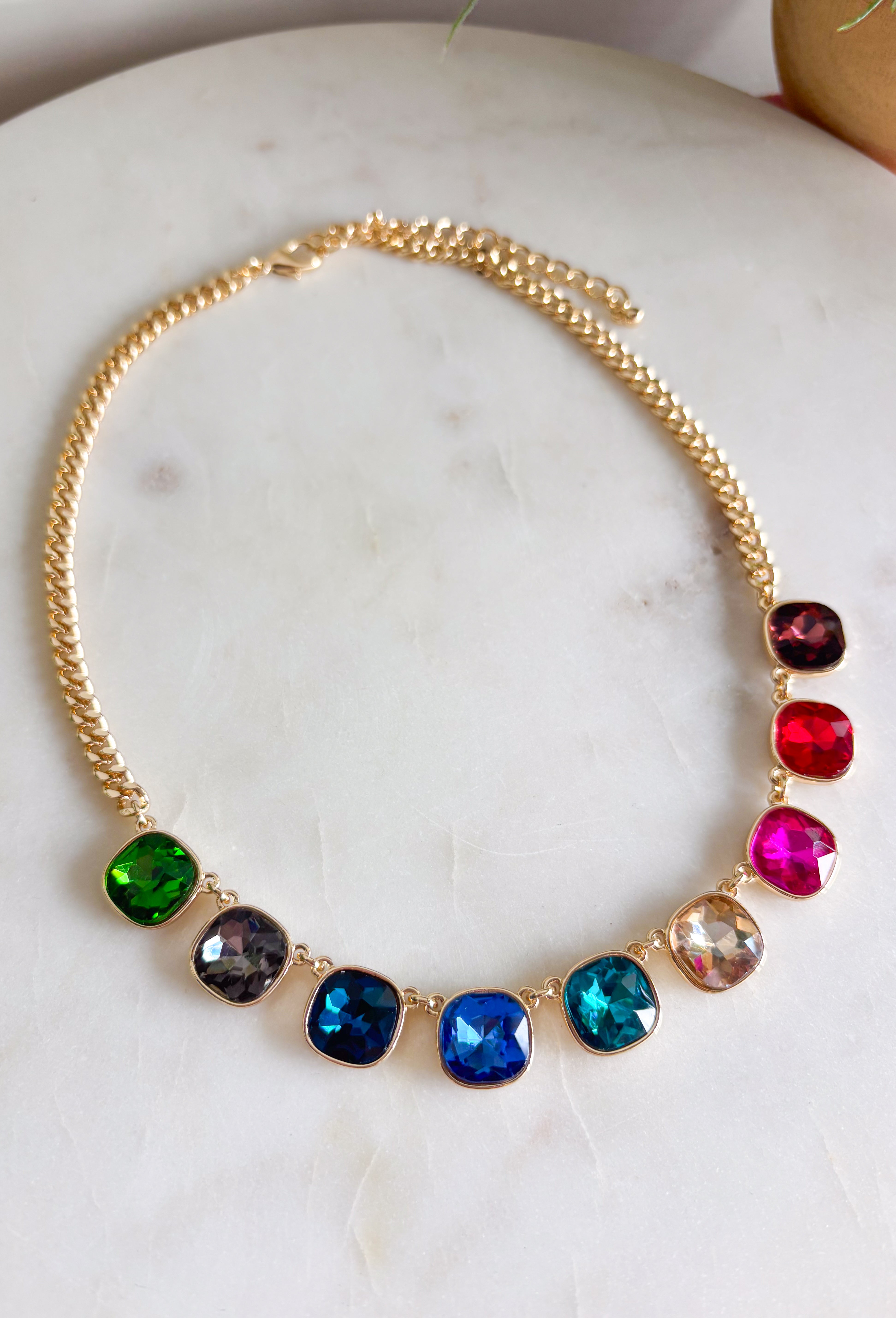 Add a vibrant finishing touch to your jewelry collection with this stunning gold chain necklace. Featuring colorful gemstones in shades of green, blue, gold, pink, red, and burgundy, this chic piece brings the perfect balance of timeless style and playful color. The delicate gold chain makes it easy to wear on its own or layered with your favorite necklaces, creating an effortlessly polished look for any occasion.