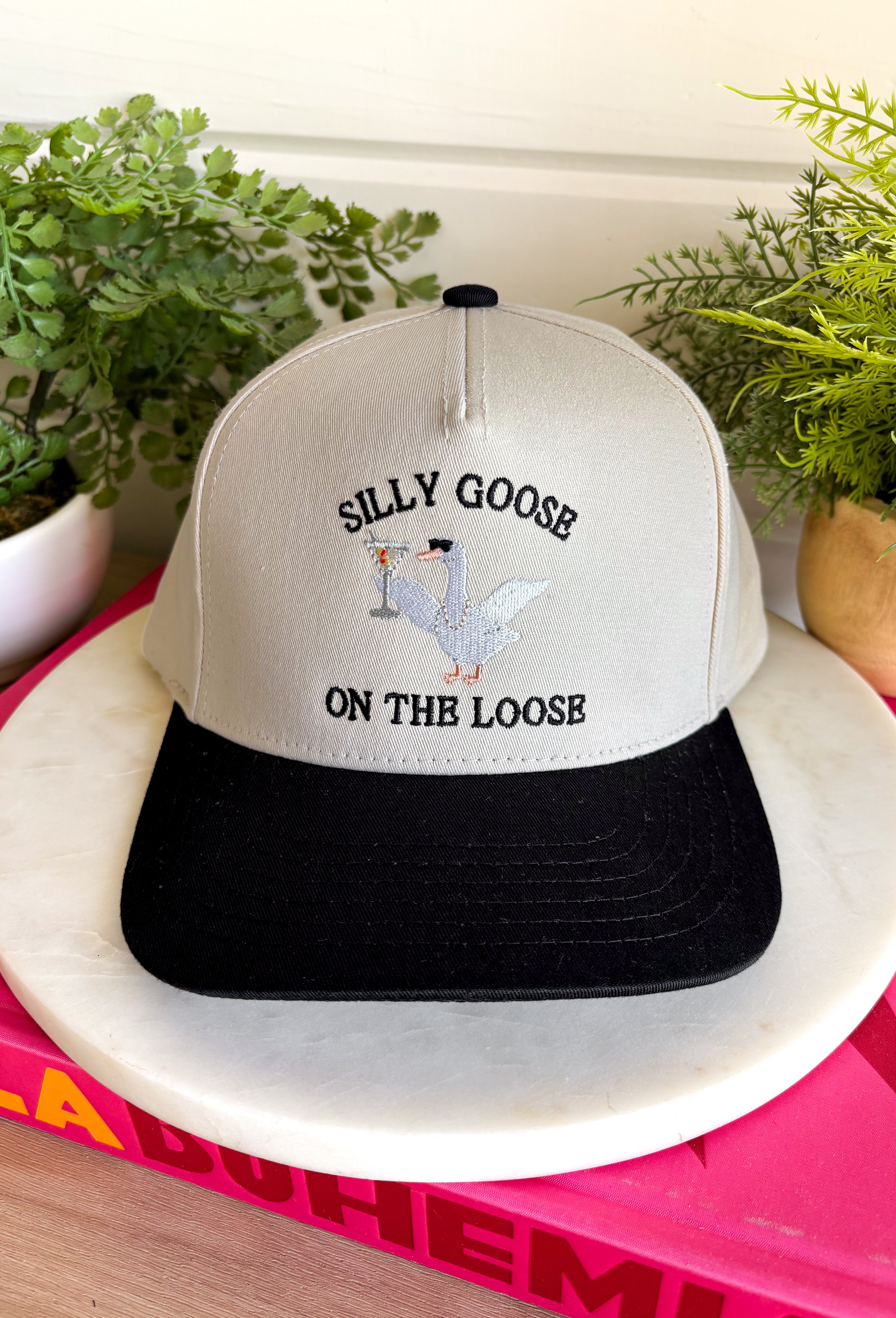 This trucker hat is serving up plenty of personality! Featuring "Silly Goose On The Loose" embroidered across the front, it's finished with the cutest white goose rocking pearls, sunglasses, and a martini for the ultimate playful touch. The neutral crown and black bill make it easy to style with all your favorite casual looks, while the detailed embroidery gives it a fun, elevated feel. You'll constantly find yourself reaching for this hat!