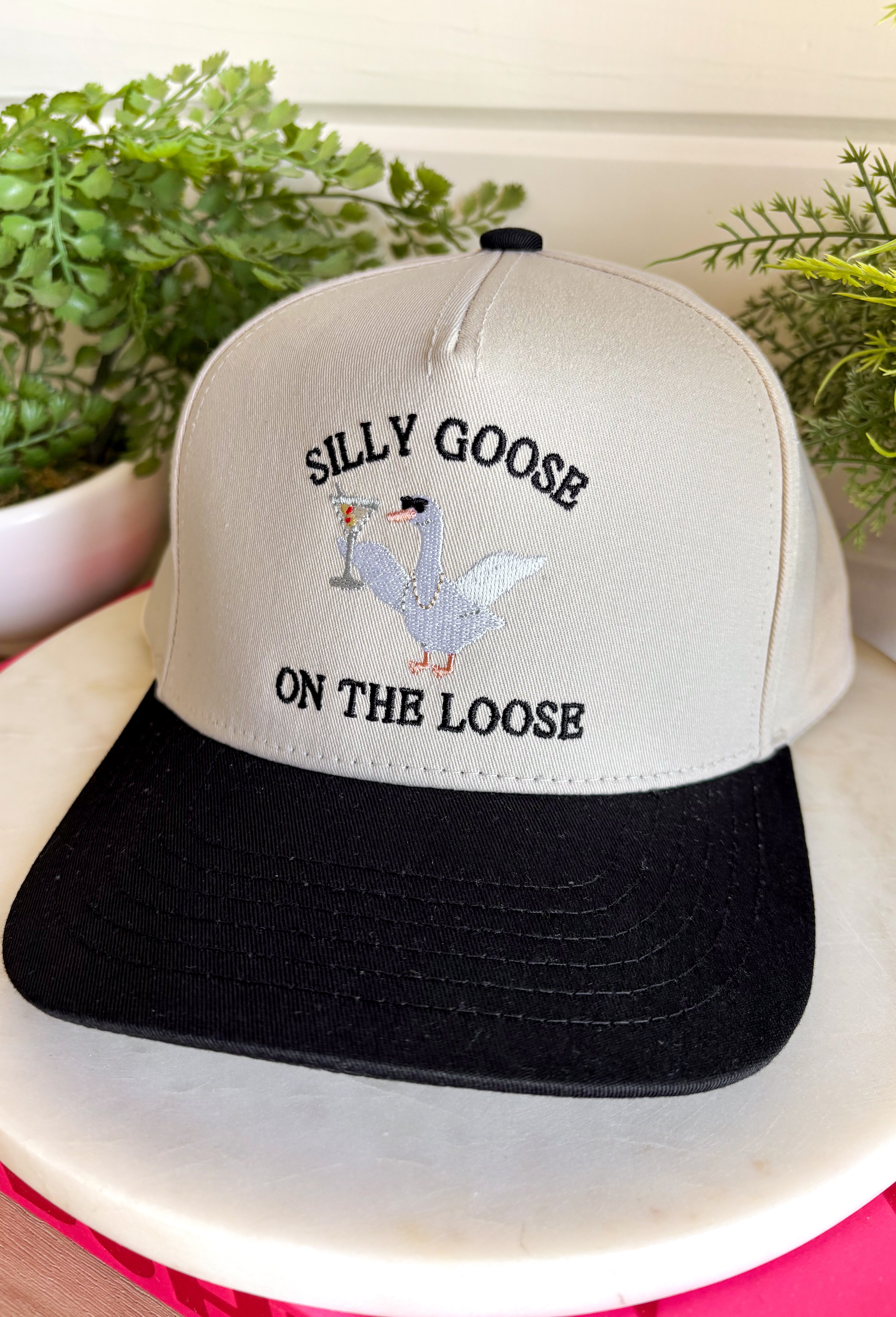 This trucker hat is serving up plenty of personality! Featuring "Silly Goose On The Loose" embroidered across the front, it's finished with the cutest white goose rocking pearls, sunglasses, and a martini for the ultimate playful touch. The neutral crown and black bill make it easy to style with all your favorite casual looks, while the detailed embroidery gives it a fun, elevated feel. You'll constantly find yourself reaching for this hat!