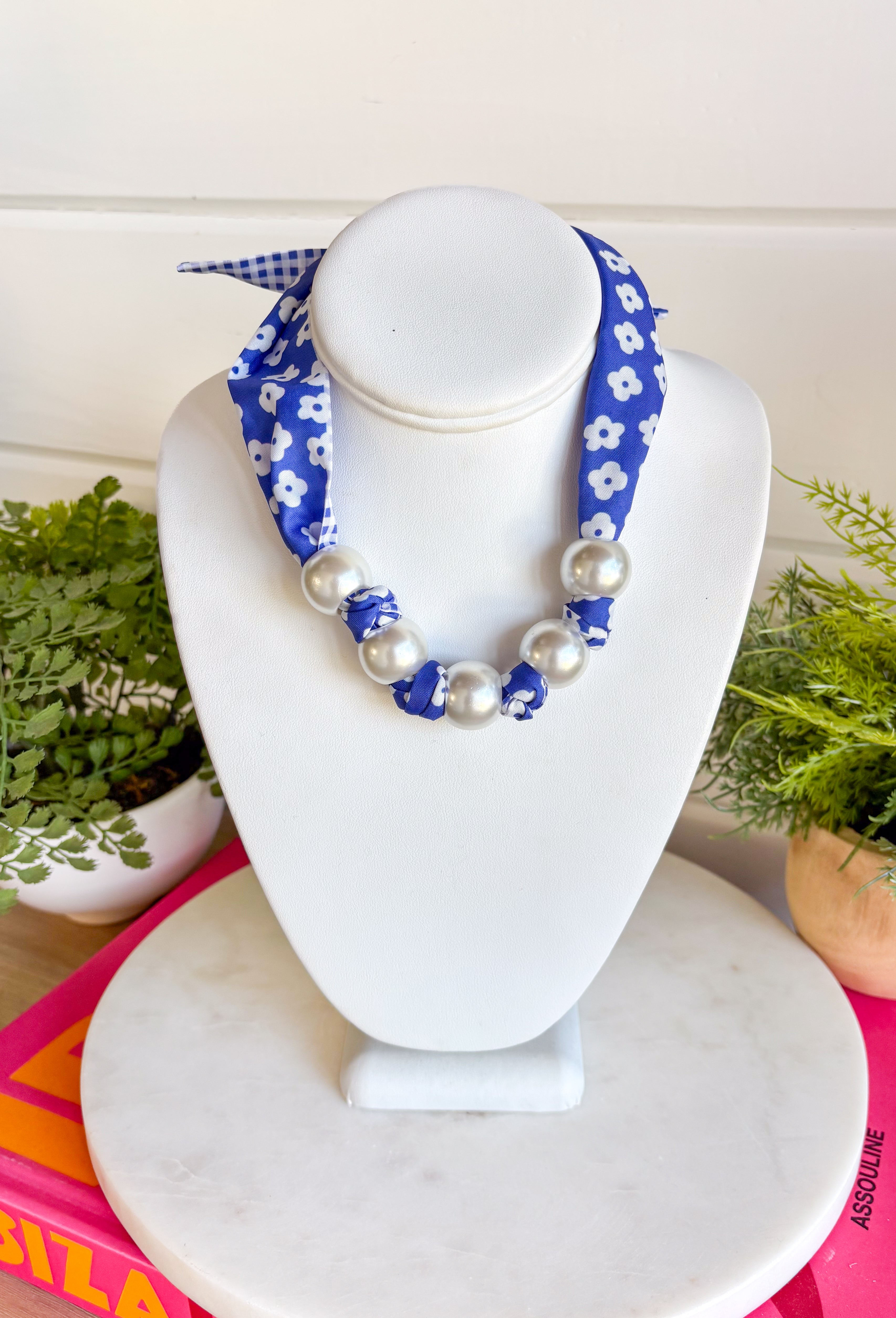 Add a fresh twist to your accessory collection with this versatile scarf necklace that's full of timeless charm. Featuring a beautiful blue and white floral print on one side and a classic blue and white gingham print on the reverse, this unique piece lets you switch up your look with ease. Chunky pearl detailing adds a chic touch, while the scarf tie design allows you to adjust the fit exactly how you like it. 
