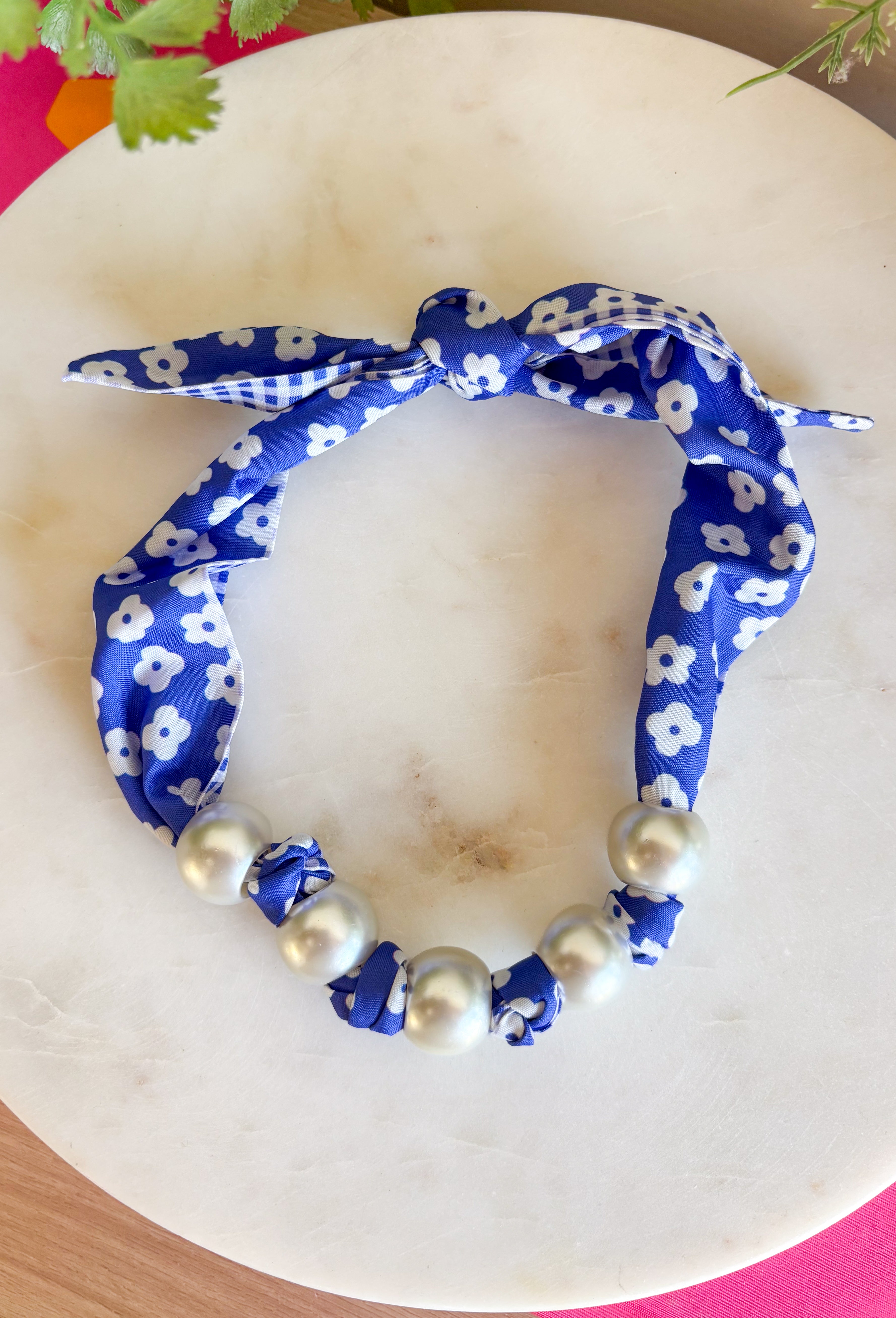 Add a fresh twist to your accessory collection with this versatile scarf necklace that's full of timeless charm. Featuring a beautiful blue and white floral print on one side and a classic blue and white gingham print on the reverse, this unique piece lets you switch up your look with ease. Chunky pearl detailing adds a chic touch, while the scarf tie design allows you to adjust the fit exactly how you like it. 