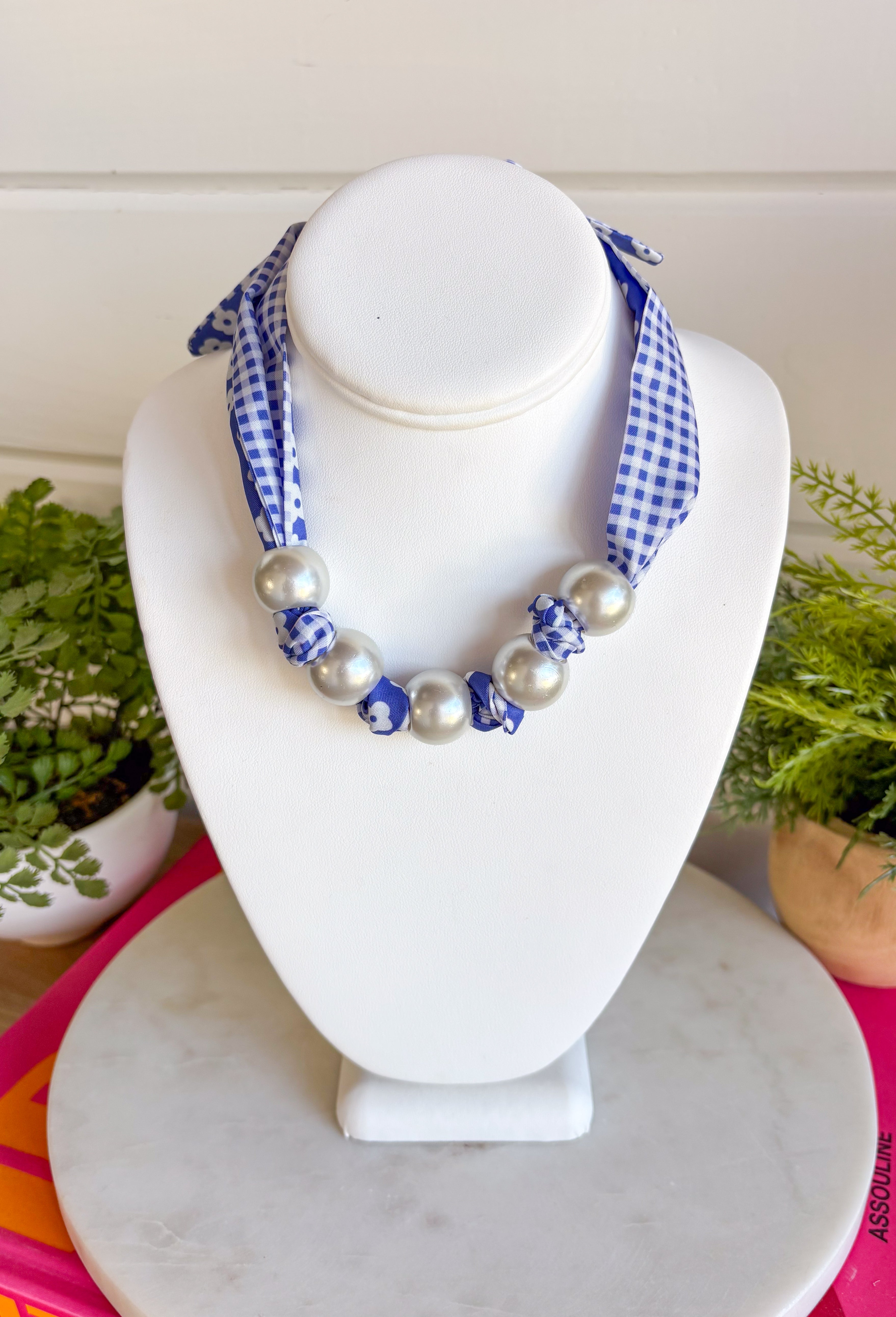 Add a fresh twist to your accessory collection with this versatile scarf necklace that's full of timeless charm. Featuring a beautiful blue and white floral print on one side and a classic blue and white gingham print on the reverse, this unique piece lets you switch up your look with ease. Chunky pearl detailing adds a chic touch, while the scarf tie design allows you to adjust the fit exactly how you like it. 