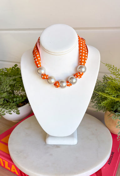 Add a playful pop of autumn color to your accessory collection with this versatile scarf necklace that's full of timeless charm. Featuring a cheerful orange polka dot print accented with brown and light pink trim, this unique piece is finished with chunky pearl detailing for a chic touch. The scarf tie design allows you to adjust the fit exactly how you like it, making it easy to wear as a necklace or wrap around your wrist as a chic bracelet. 