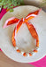 Add a playful pop of autumn color to your accessory collection with this versatile scarf necklace that's full of timeless charm. Featuring a cheerful orange polka dot print accented with brown and light pink trim, this unique piece is finished with chunky pearl detailing for a chic touch. The scarf tie design allows you to adjust the fit exactly how you like it, making it easy to wear as a necklace or wrap around your wrist as a chic bracelet.