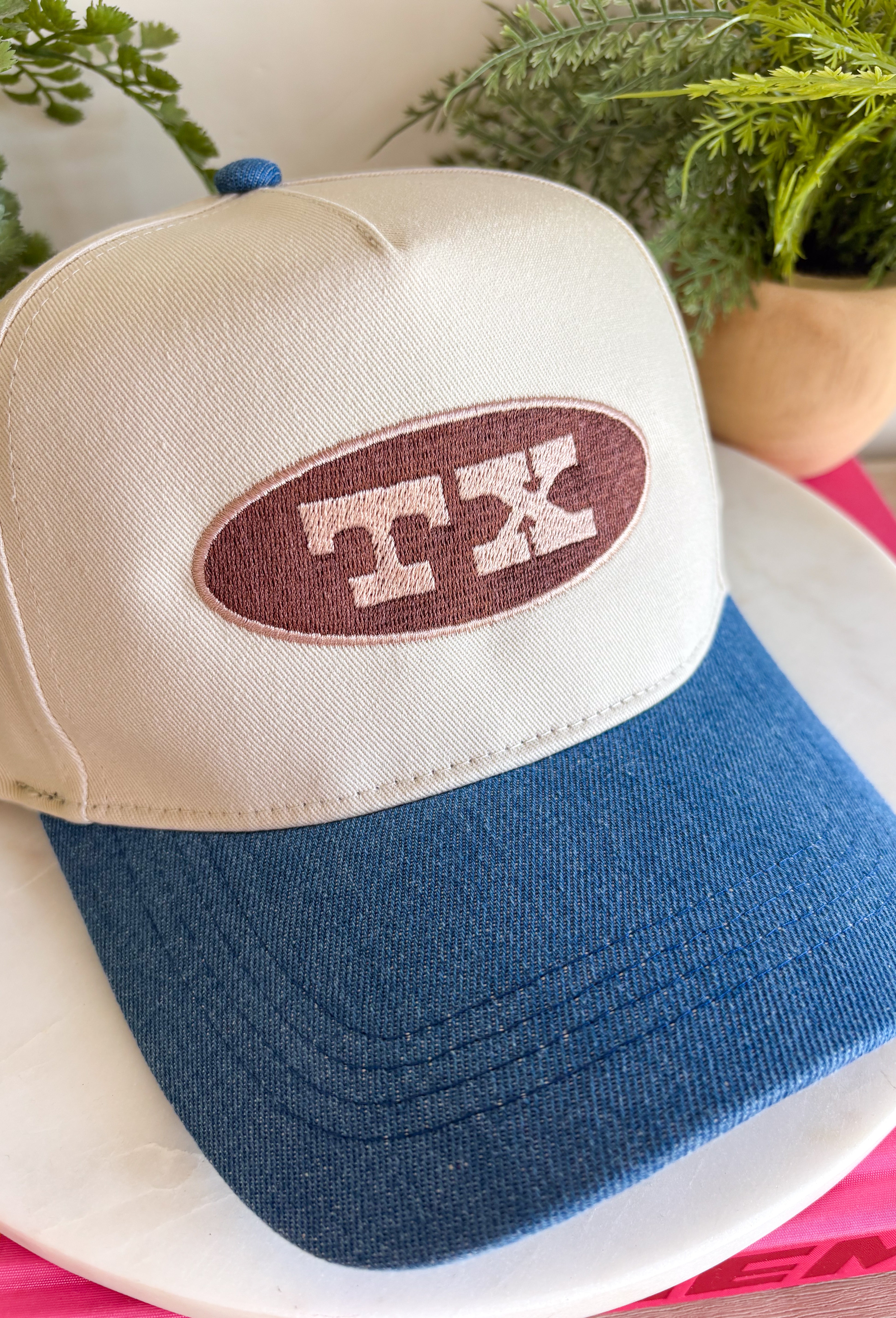Simple, timeless, and full of Texas pride! This neutral trucker hat is the perfect everyday accessory for anyone who loves the Lone Star State. Featuring a brown embroidered patch outlined in tan with a bold "TX" design, it pairs effortlessly with everything from graphic tees to cozy sweatshirts. The denim bill adds a laid-back touch, while the adjustable back ensures a comfortable fit for all-day wear.