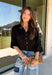 Every wardrobe needs a timeless black blouse, and this versatile top from Entro is one you'll reach for again and again. Designed with a flattering v-neckline and button-front closure, this effortlessly polished piece transitions seamlessly from workdays to weekends. The ¾ roll-tab sleeves offer versatile styling, while the elasticized smocked back hem creates a comfortable fit with a modern touch. 