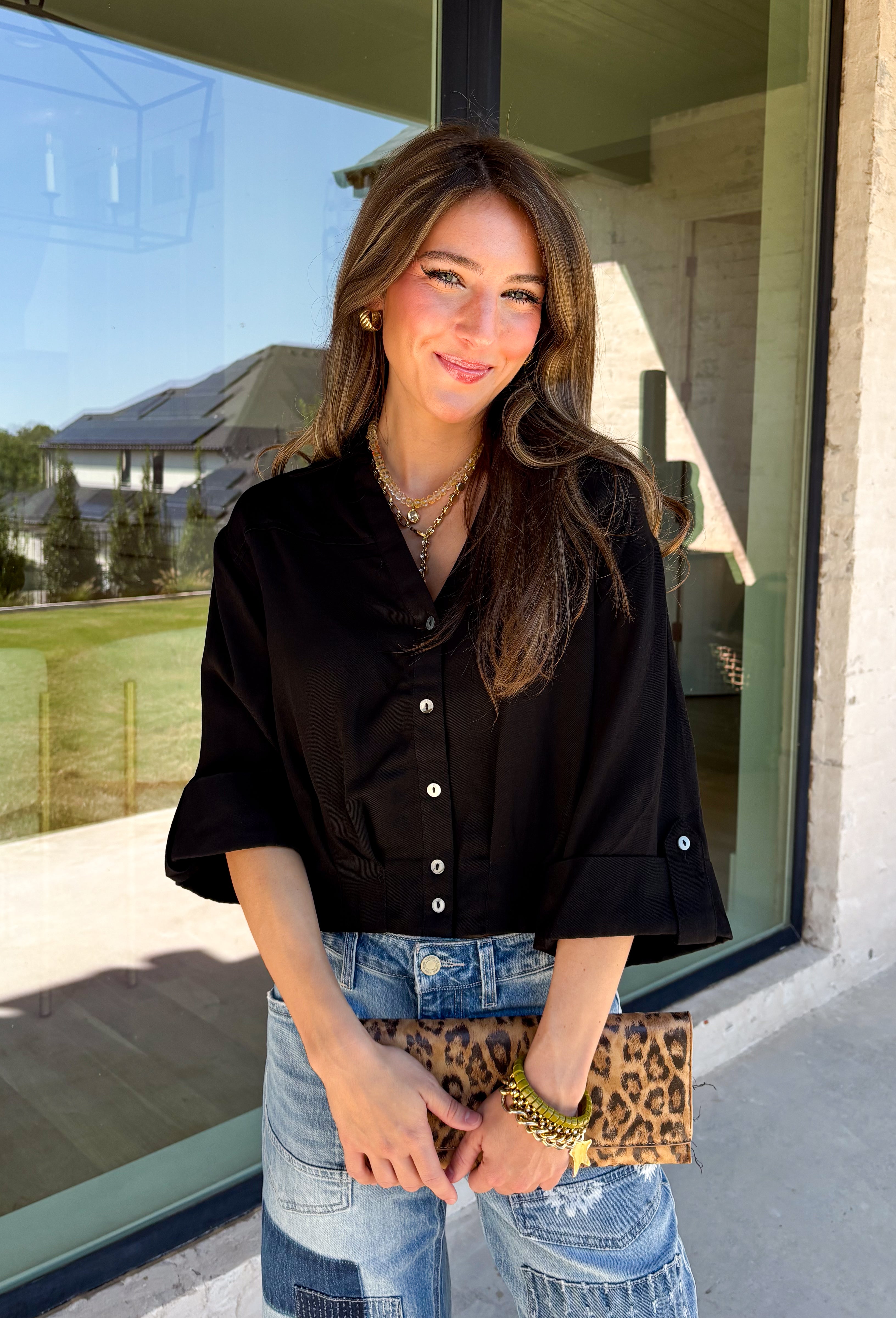 Every wardrobe needs a timeless black blouse, and this versatile top from Entro is one you'll reach for again and again. Designed with a flattering v-neckline and button-front closure, this effortlessly polished piece transitions seamlessly from workdays to weekends. The ¾ roll-tab sleeves offer versatile styling, while the elasticized smocked back hem creates a comfortable fit with a modern touch. 