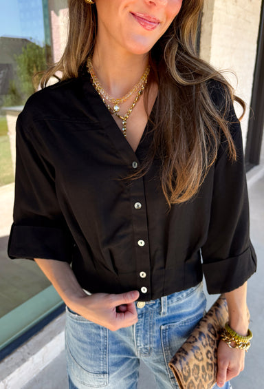 Every wardrobe needs a timeless black blouse, and this versatile top from Entro is one you'll reach for again and again. Designed with a flattering v-neckline and button-front closure, this effortlessly polished piece transitions seamlessly from workdays to weekends. The ¾ roll-tab sleeves offer versatile styling, while the elasticized smocked back hem creates a comfortable fit with a modern touch. 