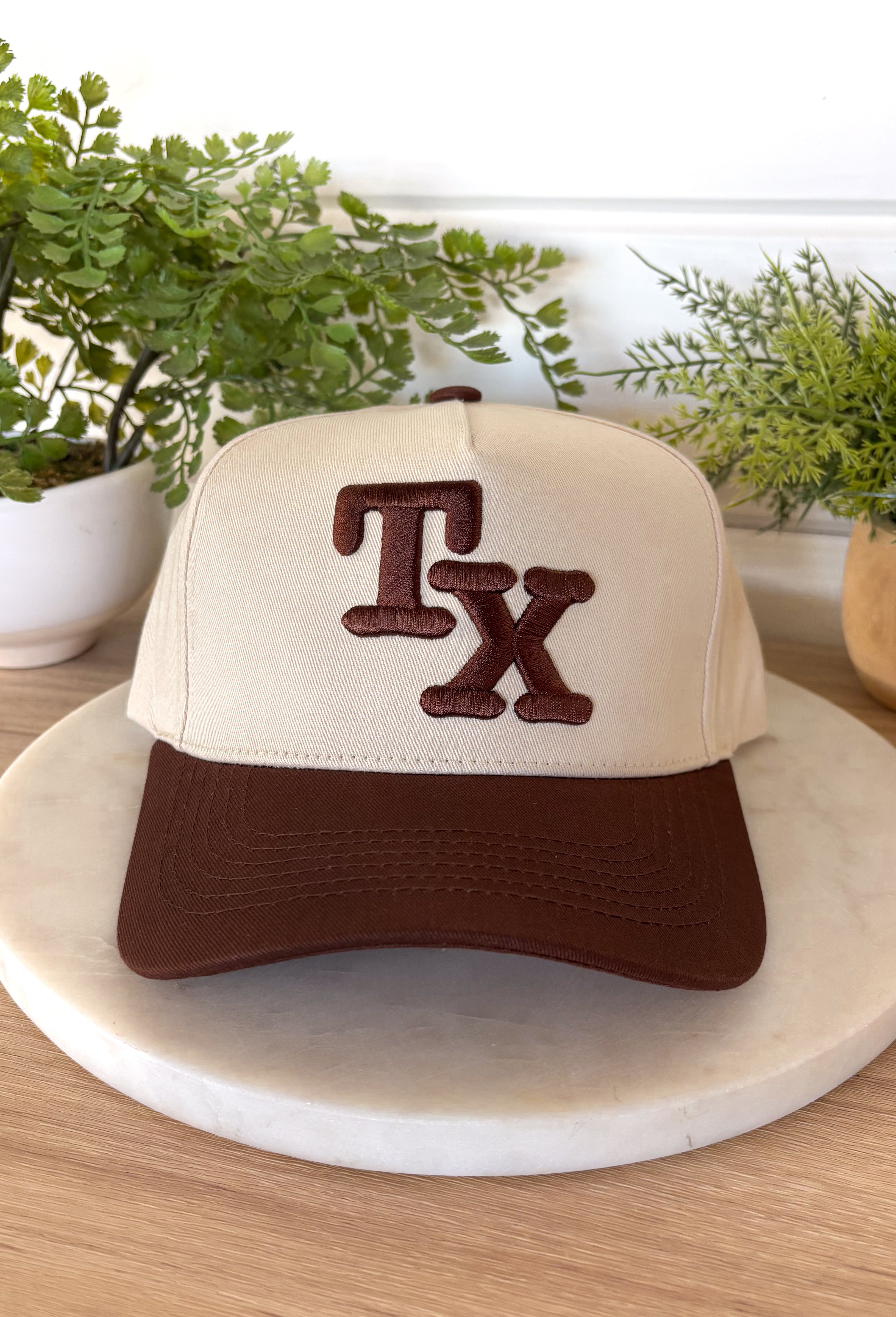 This neutral trucker hat is a timeless everyday staple with a subtle western touch. Designed with a brown bill and matching brown embroidered “TX” on the front, it keeps things classic, clean, and easy to style. The neutral color palette pairs effortlessly with just about anything, while the adjustable back ensures a comfortable, custom fit. Perfect for casual days, road trips, or showing a little Texas pride year-round.