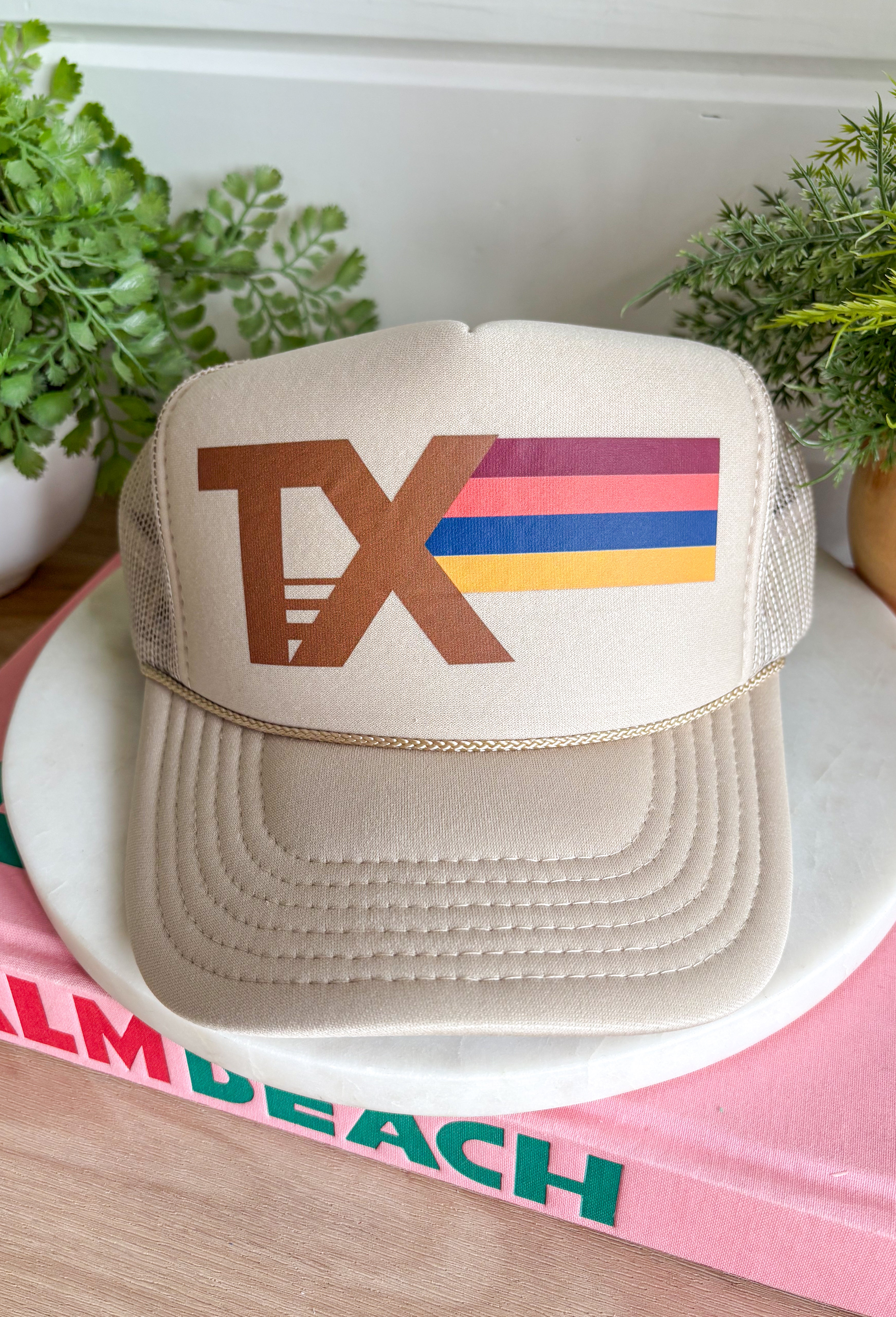 Top off your fall outfits with this timeless trucker hat featuring a classic brown "TX" graphic with a beautiful fall-inspired print. The neutral tan crown makes it easy to pair with all your favorite seasonal looks, while the rich autumn shades add the perfect pop of color. Designed with a breathable mesh back and an adjustable fit, this hat is made for everything from pumpkin patch visits and football weekends to running errands around town. 