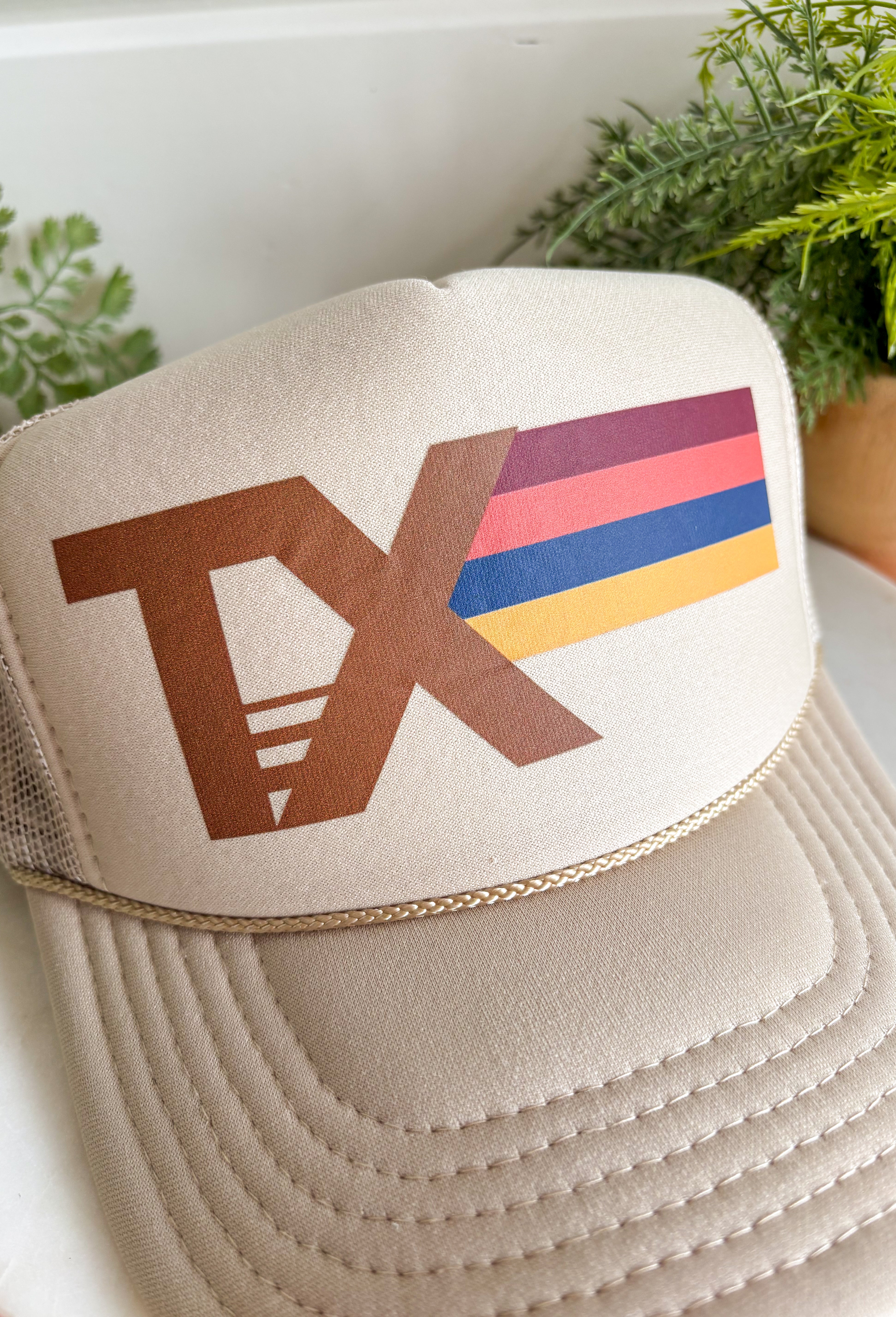 Top off your fall outfits with this timeless trucker hat featuring a classic brown "TX" graphic with a beautiful fall-inspired print. The neutral tan crown makes it easy to pair with all your favorite seasonal looks, while the rich autumn shades add the perfect pop of color. Designed with a breathable mesh back and an adjustable fit, this hat is made for everything from pumpkin patch visits and football weekends to running errands around town. 