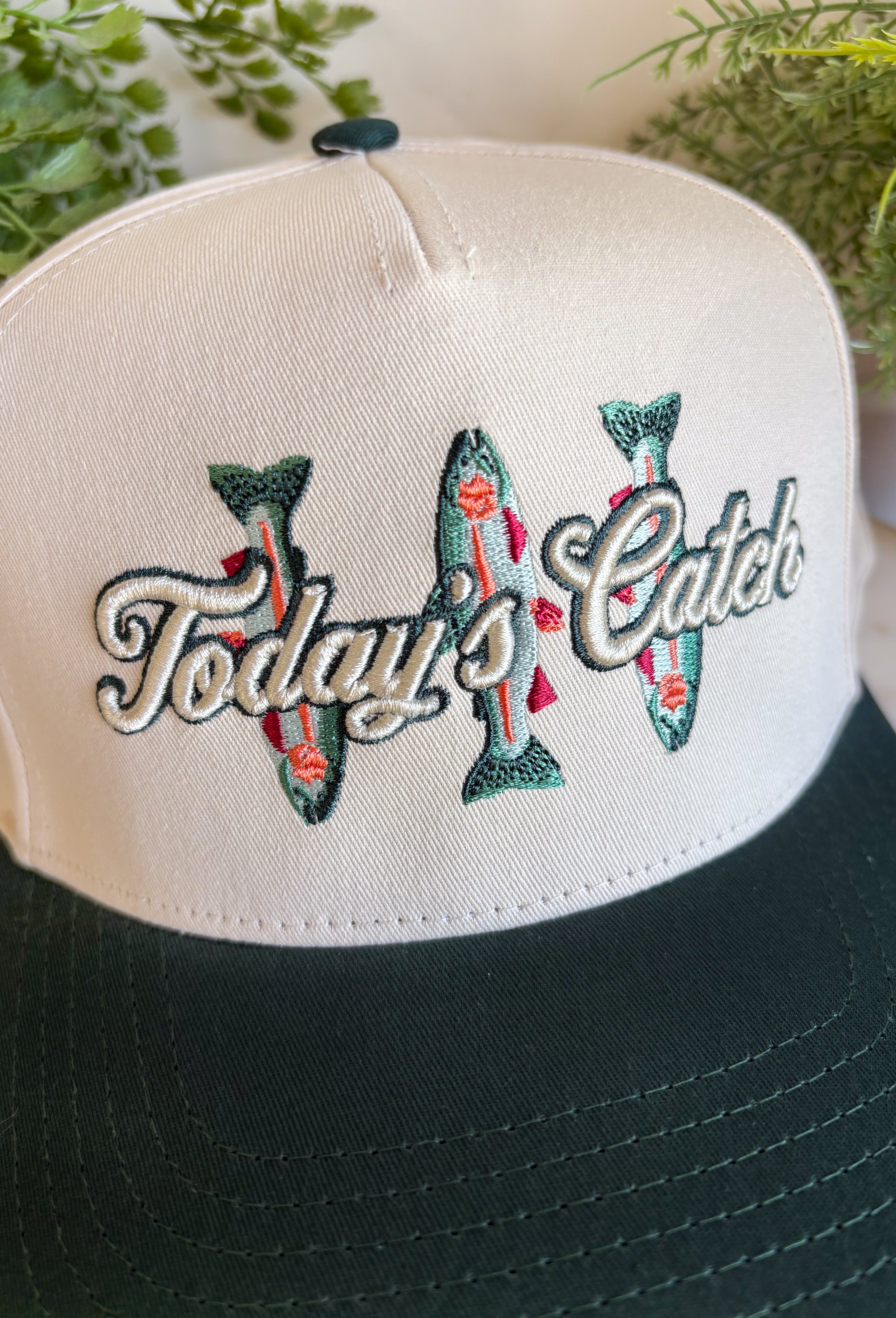 Whether you're headed to the lake, spending the day outdoors, or just love a playful graphic accessory, this trucker hat from The Happiest is the perfect finishing touch. Featuring a neutral crown with a hunter green bill, this hat is embroidered with "Today's Catch" and a colorful fish design in shades of green, blue, and pink for a fun, laid-back look. The adjustable fit makes it comfortable for all-day wear, making it an easy grab-and-go accessory for every adventure.