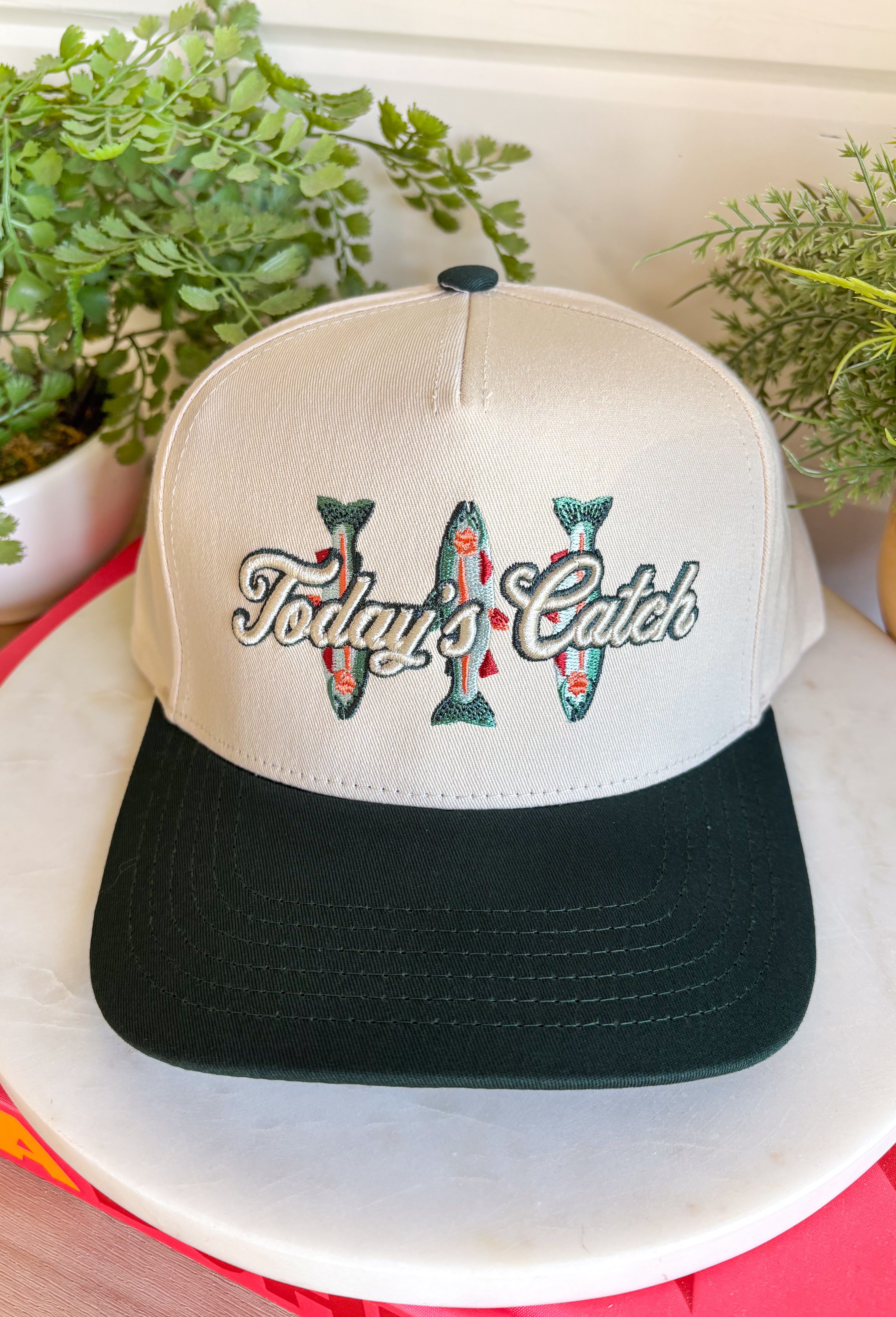 Whether you're headed to the lake, spending the day outdoors, or just love a playful graphic accessory, this trucker hat from The Happiest is the perfect finishing touch. Featuring a neutral crown with a hunter green bill, this hat is embroidered with "Today's Catch" and a colorful fish design in shades of green, blue, and pink for a fun, laid-back look. The adjustable fit makes it comfortable for all-day wear, making it an easy grab-and-go accessory for every adventure.
