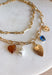 Turn any outfit into a statement with this chunky gold layered chain necklace. The double-layer design creates an effortless stacked look, while the second chain features an assortment of charming details — textured gold hearts, a pearl accent, a blue rhinestone, and a tan heart charm. It’s the perfect mix of bold and feminine, making it a go-to accessory for all season long.