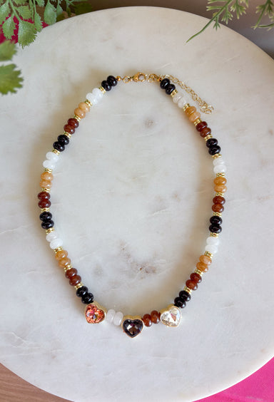 Warm earthy tones and shimmering details make this handcrafted necklace a standout accessory for every season! Featuring rich brown, and neutral beads accented with gold details, this chic piece is finished with sparkling heart-cut crystals that add just the right amount of sparkle. Whether you're dressing up a cozy sweater or adding a special touch to your favorite dress, this necklace is a timeless piece you'll reach for again and again.