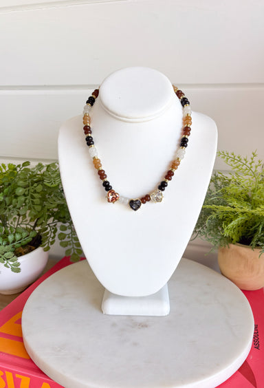 Warm earthy tones and shimmering details make this handcrafted necklace a standout accessory for every season! Featuring rich brown, and neutral beads accented with gold details, this chic piece is finished with sparkling heart-cut crystals that add just the right amount of sparkle. Whether you're dressing up a cozy sweater or adding a special touch to your favorite dress, this necklace is a timeless piece you'll reach for again and again.