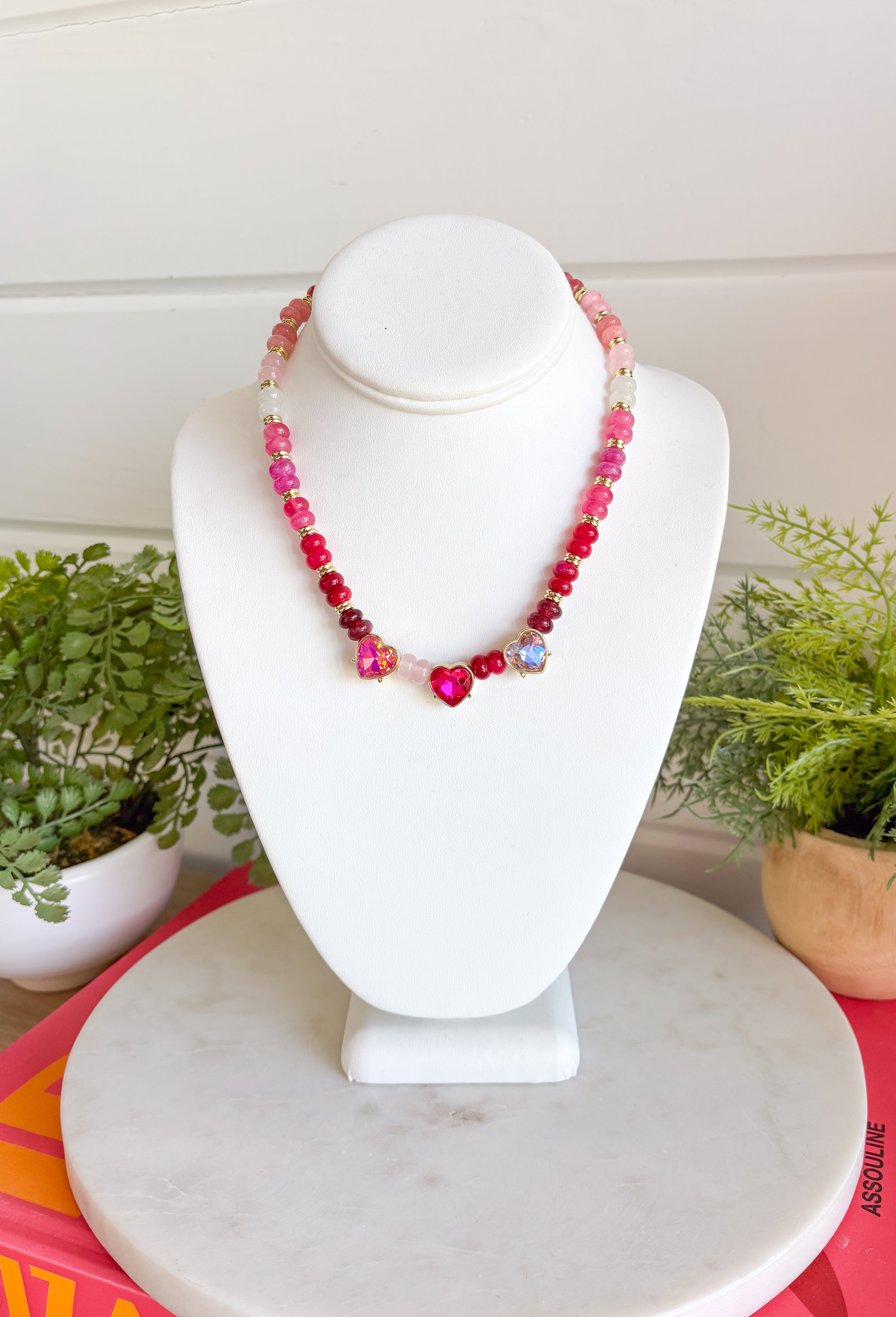 Warm shades of pink and shimmering details make this handcrafted necklace a standout accessory for every season! Featuring beautiful pink beads in a variety of tones accented with gold details, this elegant piece is finished with sparkling heart-cut crystals that add the perfect touch of brilliance. Whether you're dressing up a cozy sweater or adding a feminine touch to your favorite dress, this timeless necklace brings cheerful color and effortless charm to every outfit.