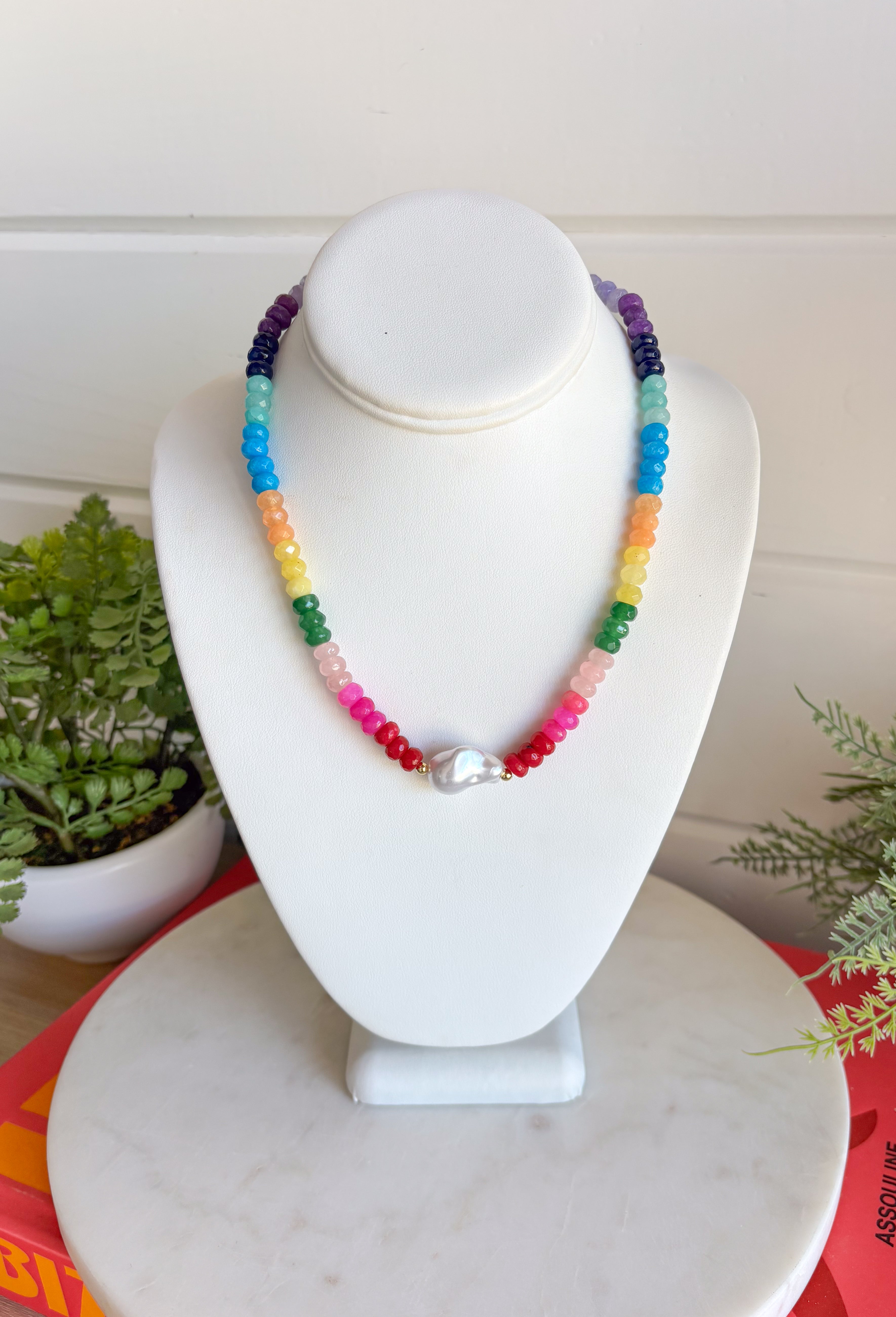 This colorful gemstone beaded necklace is pure happiness in accessory form! Featuring a mix of purple, blue, orange, yellow, green, and pink with a pearl accent, it adds the perfect playful pop to all your summer outfits. It’s bright, fun, and instantly makes even the simplest look feel styled. The shorter length sits perfectly at the neckline, making it great for layering or wearing solo as a statement.
