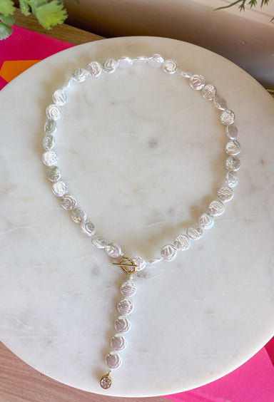 Classic pearls meet modern elegance in this stunning lariat necklace! Featuring lustrous pearls and a chic gold toggle closure, this timeless piece is finished with a sparkling rhinestone accent that adds just the right amount of shimmer. Whether you're dressing up for a holiday celebration, wedding, date night, or simply elevating your everyday style, this handcrafted necklace brings effortless sophistication to any outfit.