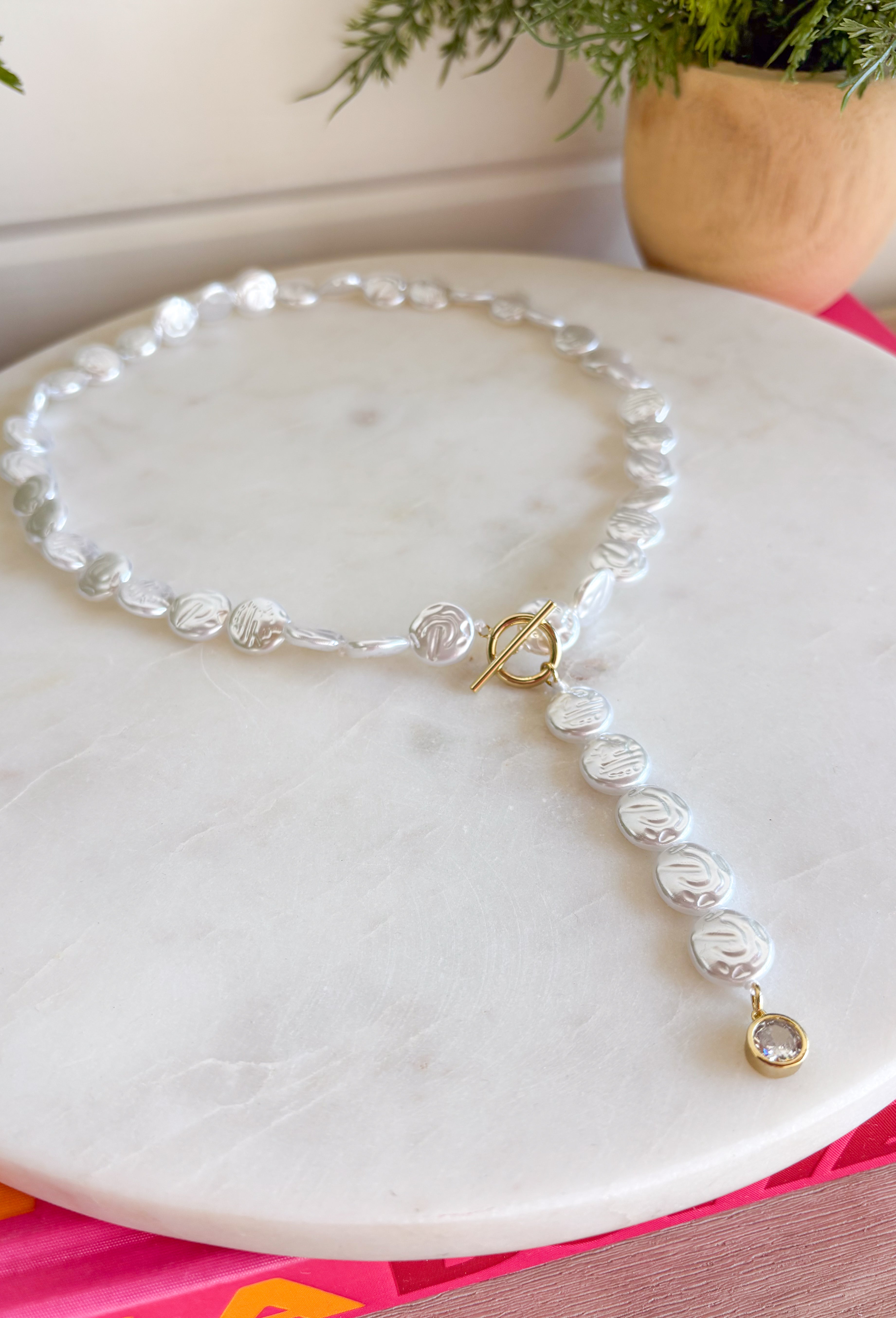Classic pearls meet modern elegance in this stunning lariat necklace! Featuring lustrous pearls and a chic gold toggle closure, this timeless piece is finished with a sparkling rhinestone accent that adds just the right amount of shimmer. Whether you're dressing up for a holiday celebration, wedding, date night, or simply elevating your everyday style, this handcrafted necklace brings effortless sophistication to any outfit.