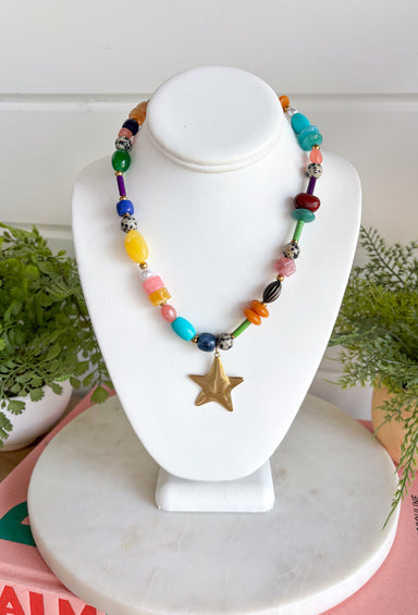 Color, texture, and a little golden shine come together in this playful necklace from Treasure Jewels. A dazzling mix of yellow, pink, blue, green, orange, gold, and spotted beads gives it a collected, one-of-a-kind feel, while the variety of shapes and textures makes every detail worth a closer look. A gold star pendant finishes the design with a fun statement at the center. Whether you’re brightening up a simple sweater or adding extra personality to a layered look, this necklace is made to stand out.