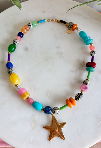 Color, texture, and a little golden shine come together in this playful necklace from Treasure Jewels. A dazzling mix of yellow, pink, blue, green, orange, gold, and spotted beads gives it a collected, one-of-a-kind feel, while the variety of shapes and textures makes every detail worth a closer look. A gold star pendant finishes the design with a fun statement at the center. Whether you’re brightening up a simple sweater or adding extra personality to a layered look, this necklace is made to stand out.